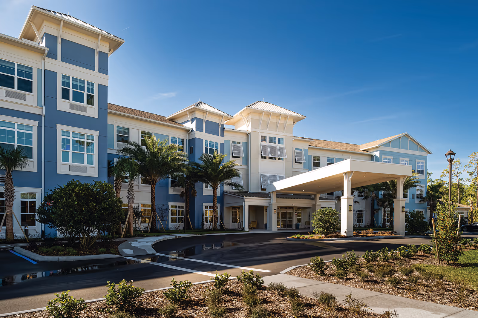 Blue and white senior living facility with a covered entrance and palm trees.