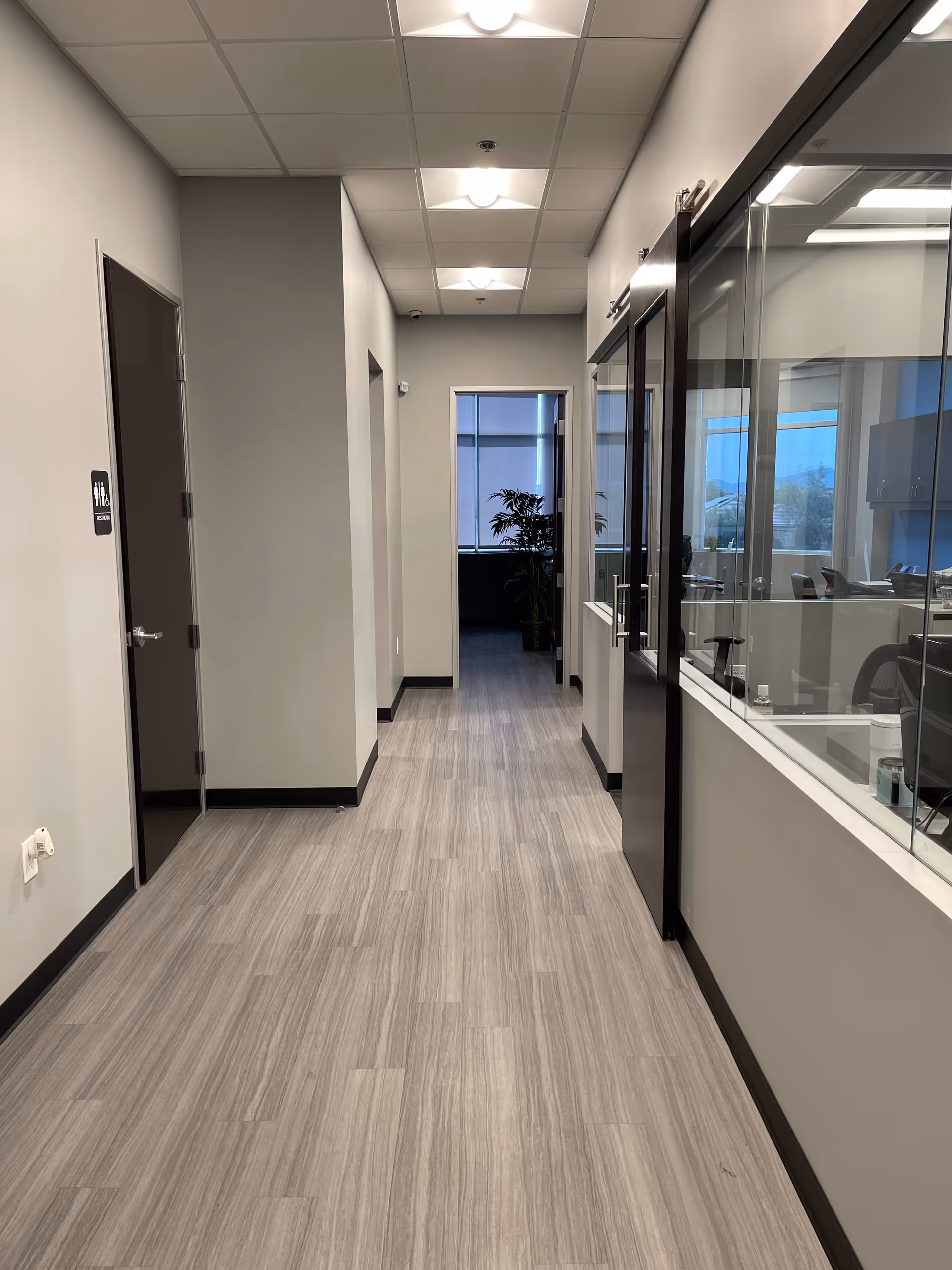 Long hallway with glass-walled offices on the right and neutral gray flooring.