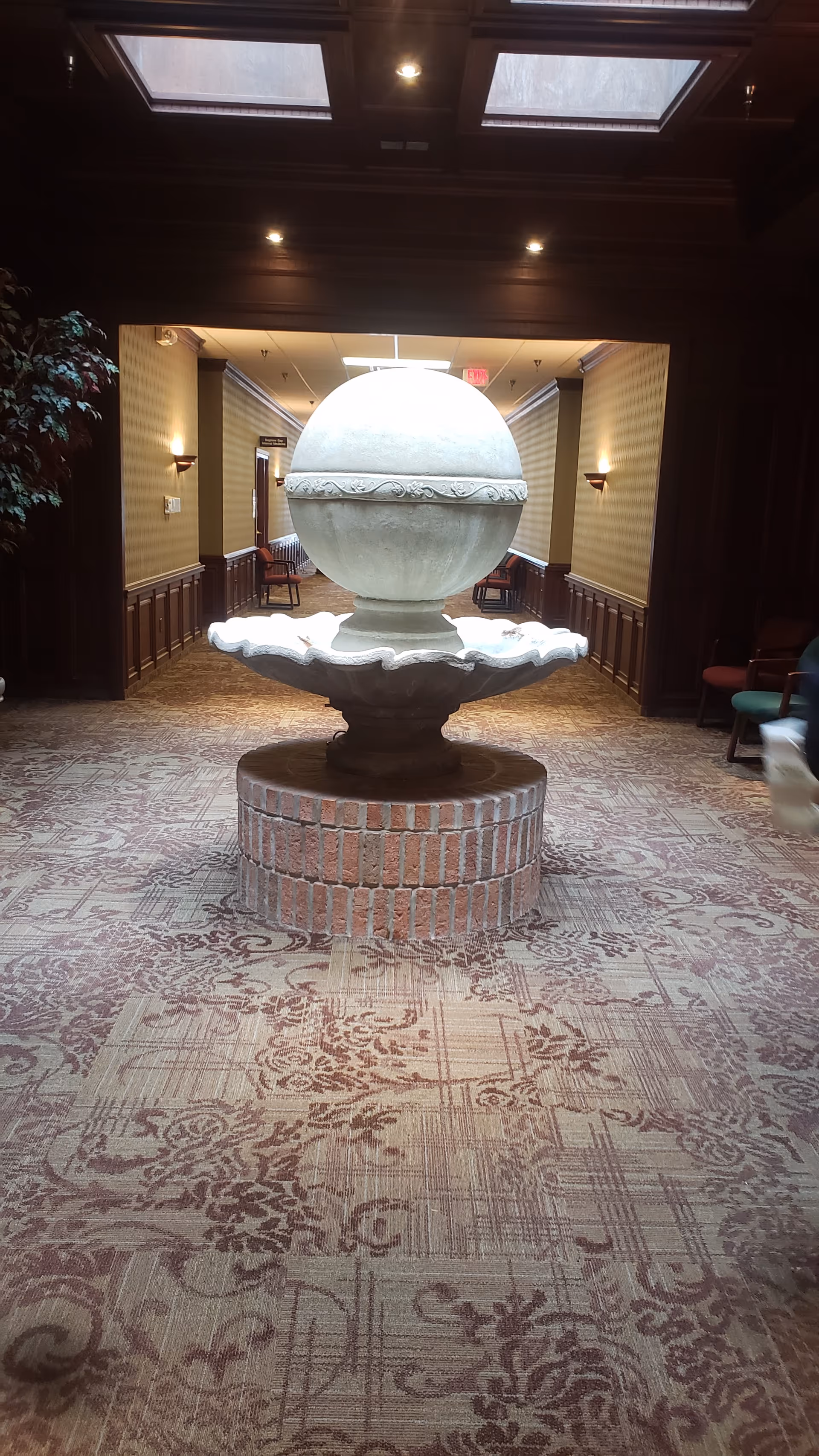 Indoor hallway featuring a central stone fountain with brick base and patterned carpet.