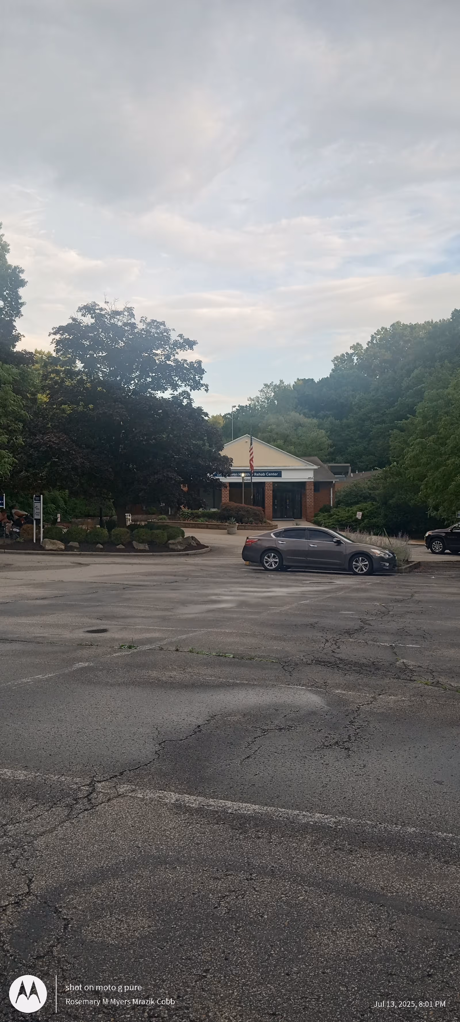 Exterior view of Woodhaven Care Center entrance with trees, parking lot, and flag.
