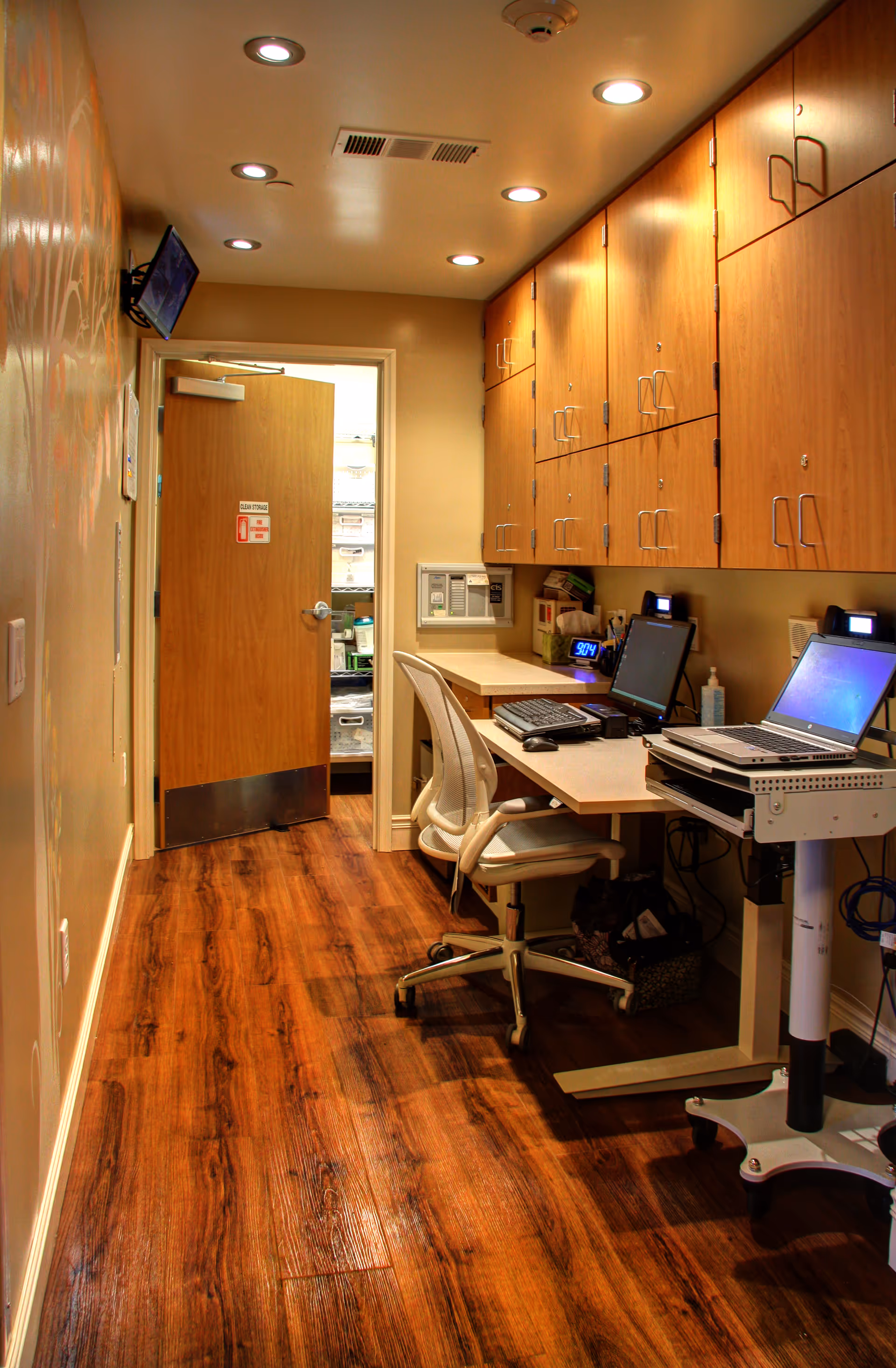 Narrow interior hallway with wood floors, cabinets, and a desk area along the right.