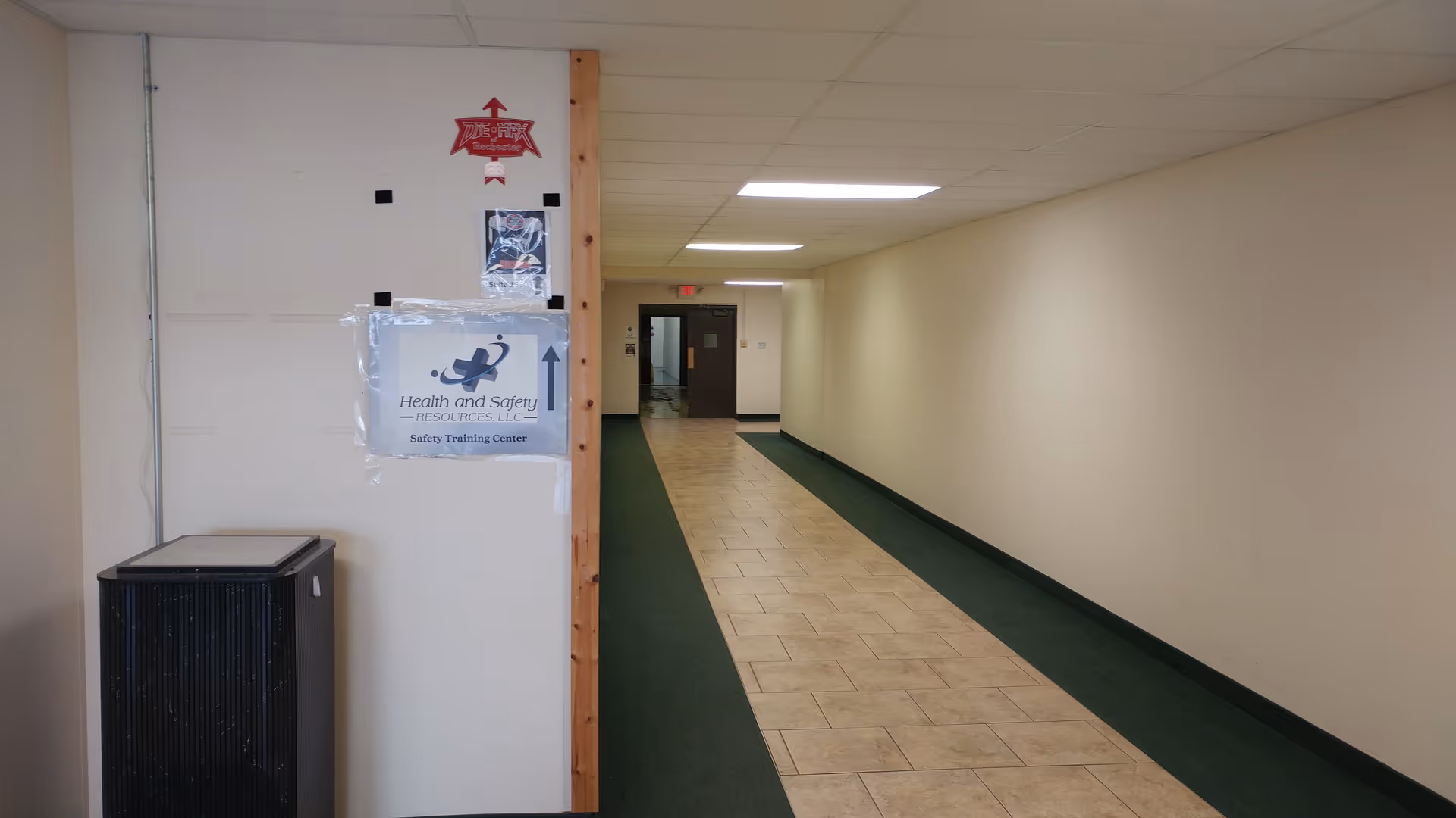Long interior hallway with tiled center and green carpet borders, wall sign visible.