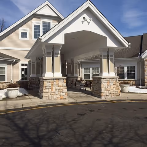 A senior living facility entrance with a covered porte-cochere supported by stone pillars and benches.