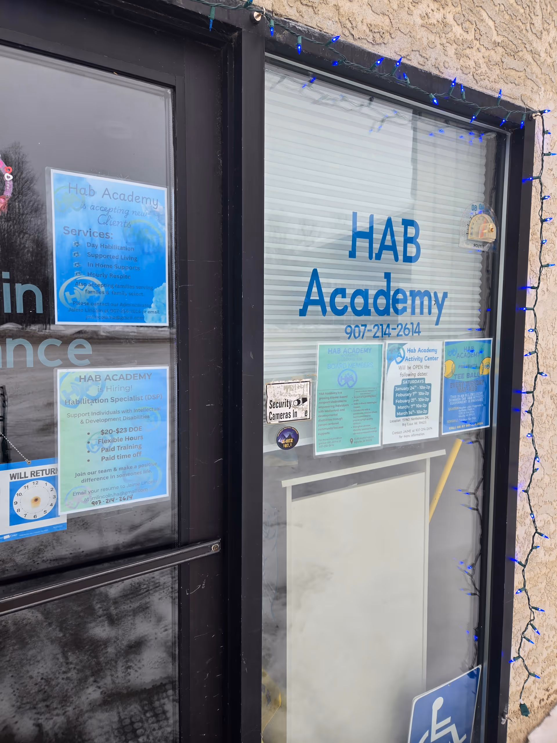 Front entrance of HAB Academy with blue signage, posters on glass, and string lights.