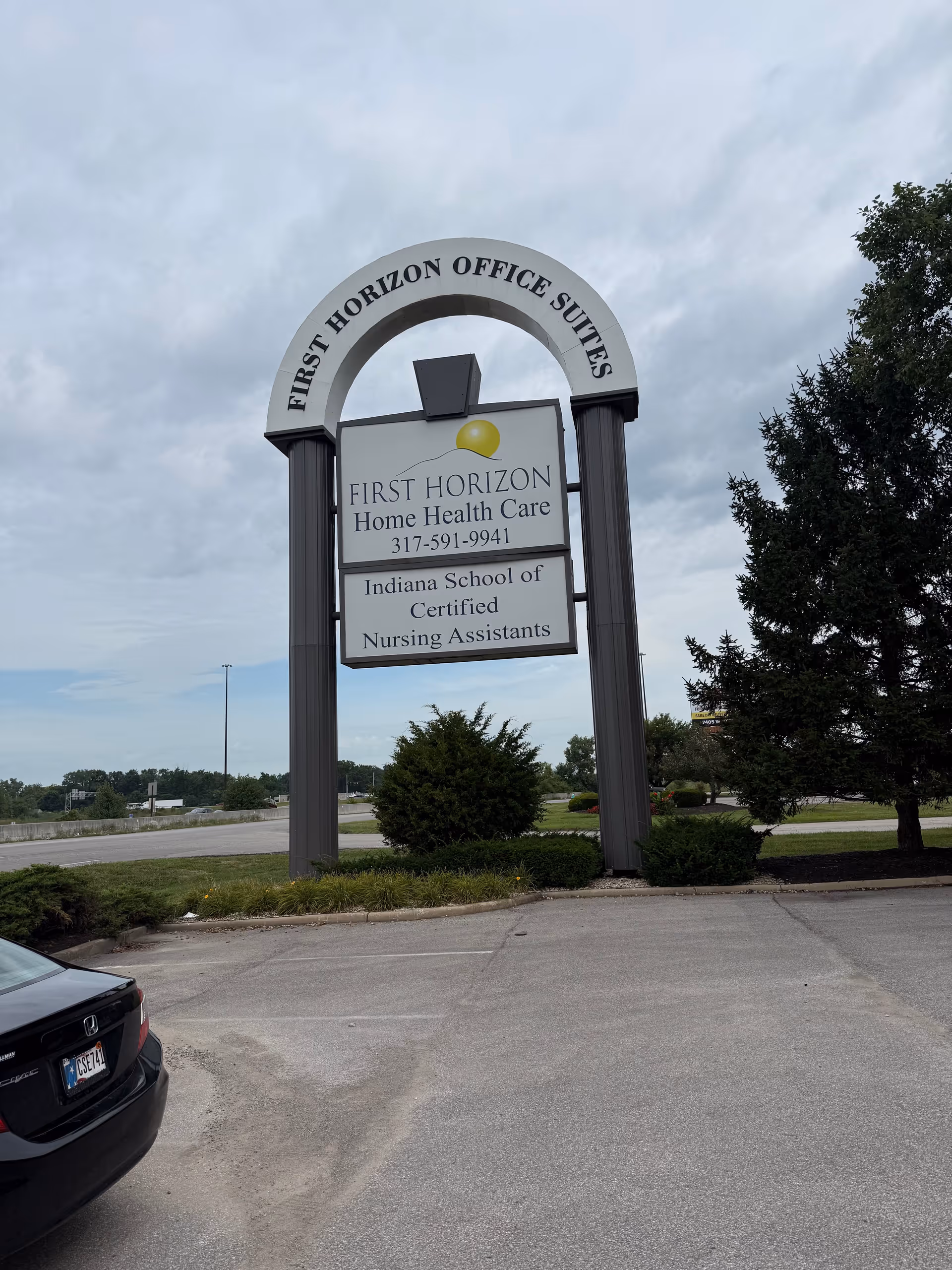 Outdoor scene featuring a large arched sign for First Horizon Office Suites in a parking lot.