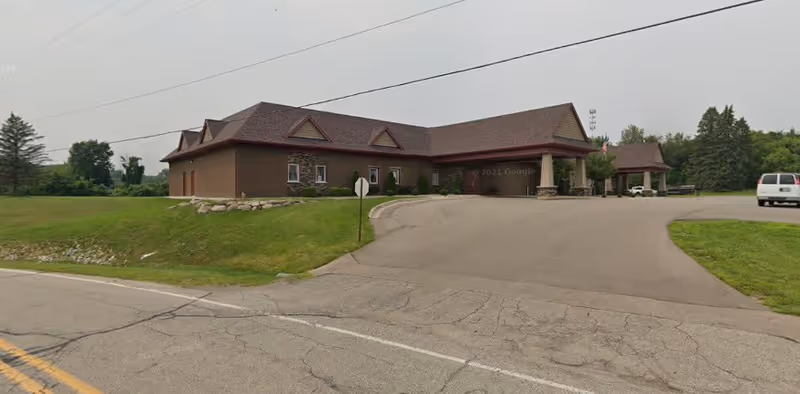 Single-story brick facility with a covered main entrance, curved driveway, and surrounding lawn.