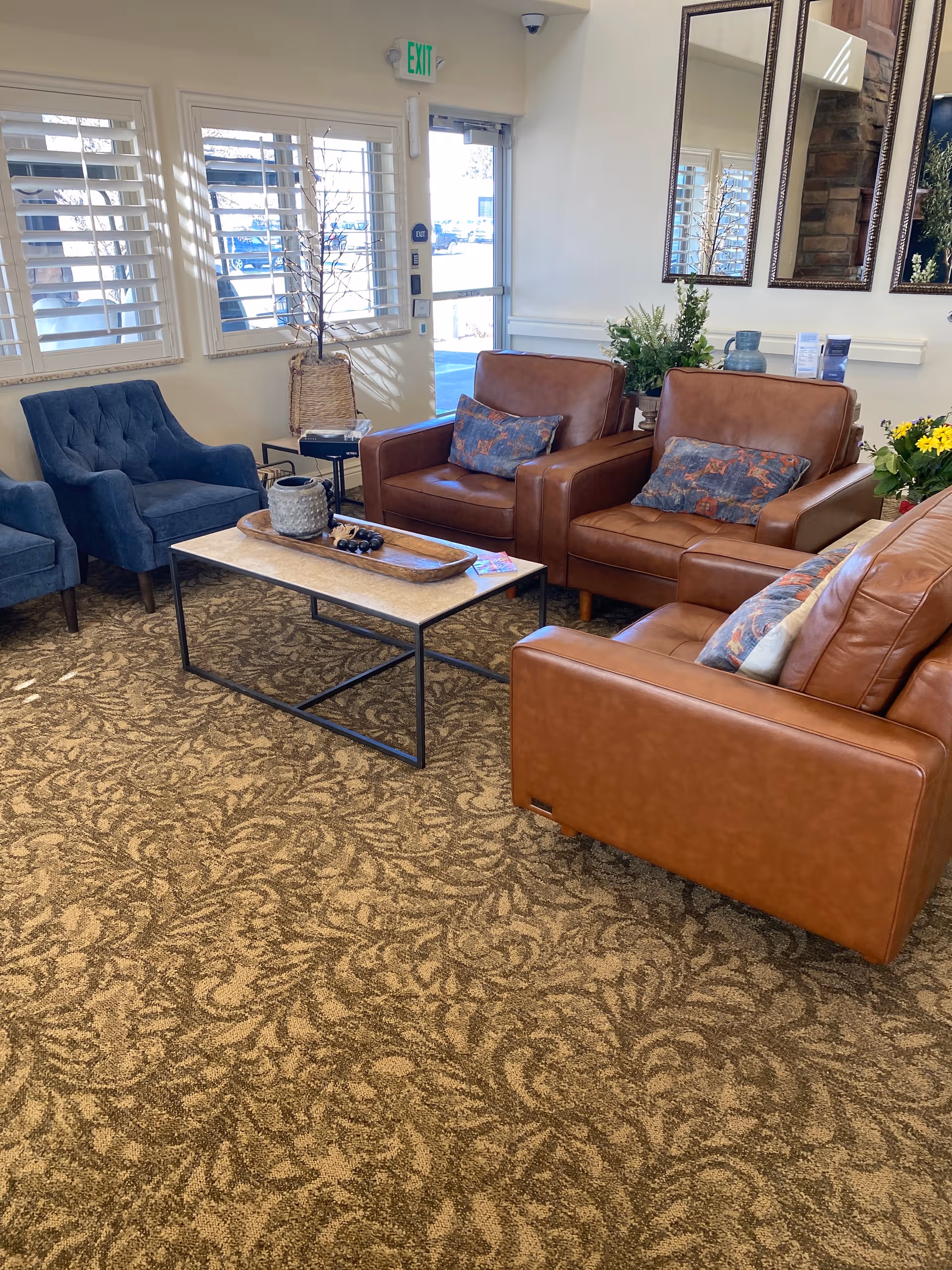 Cozy senior living lounge with blue chairs, brown leather sofas, and a coffee table.
