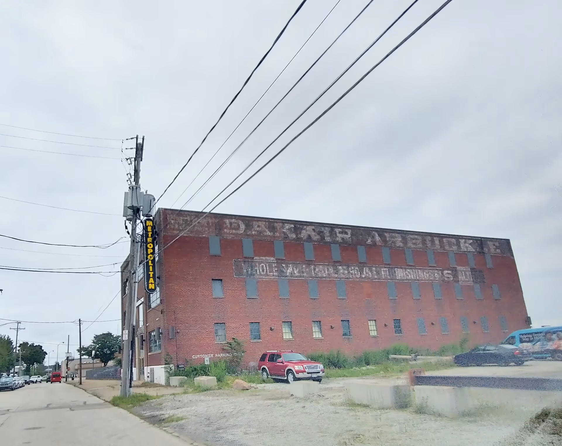 A large red brick building along a street with power lines overhead.