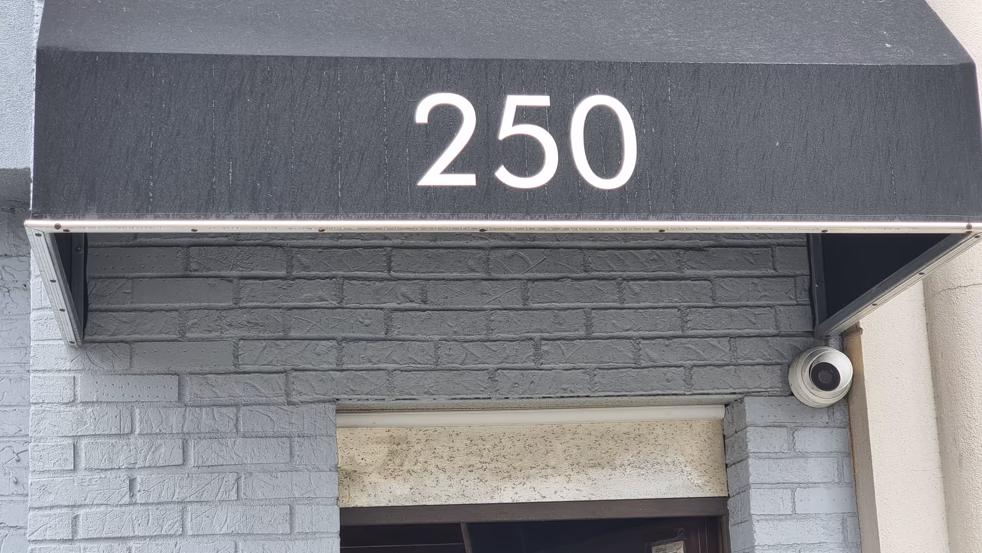 Gray brick building entrance with the number 250 and a security camera.