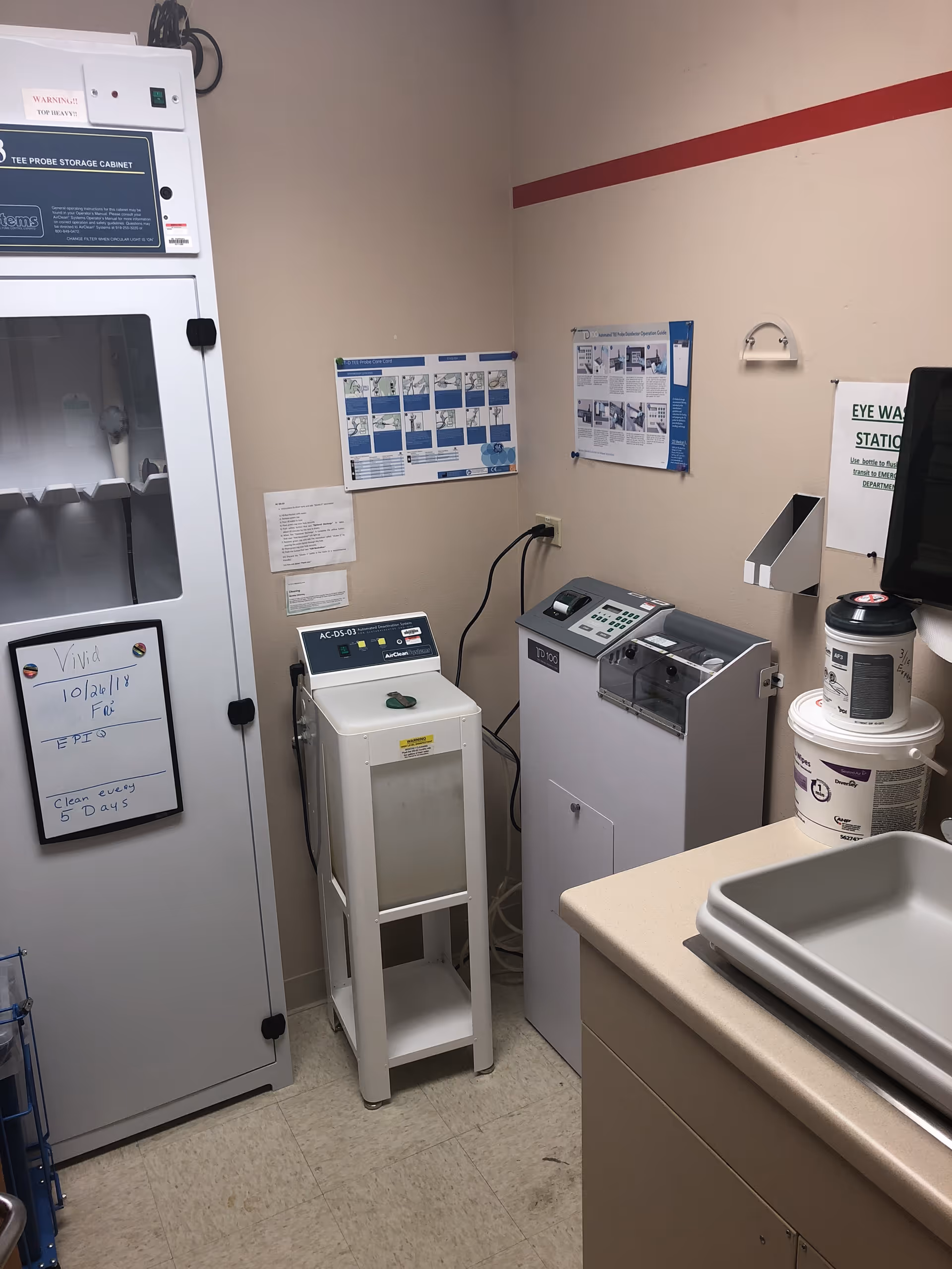 Clinical supply room with a tall storage cabinet, laundry machines, sink, and wall posters.