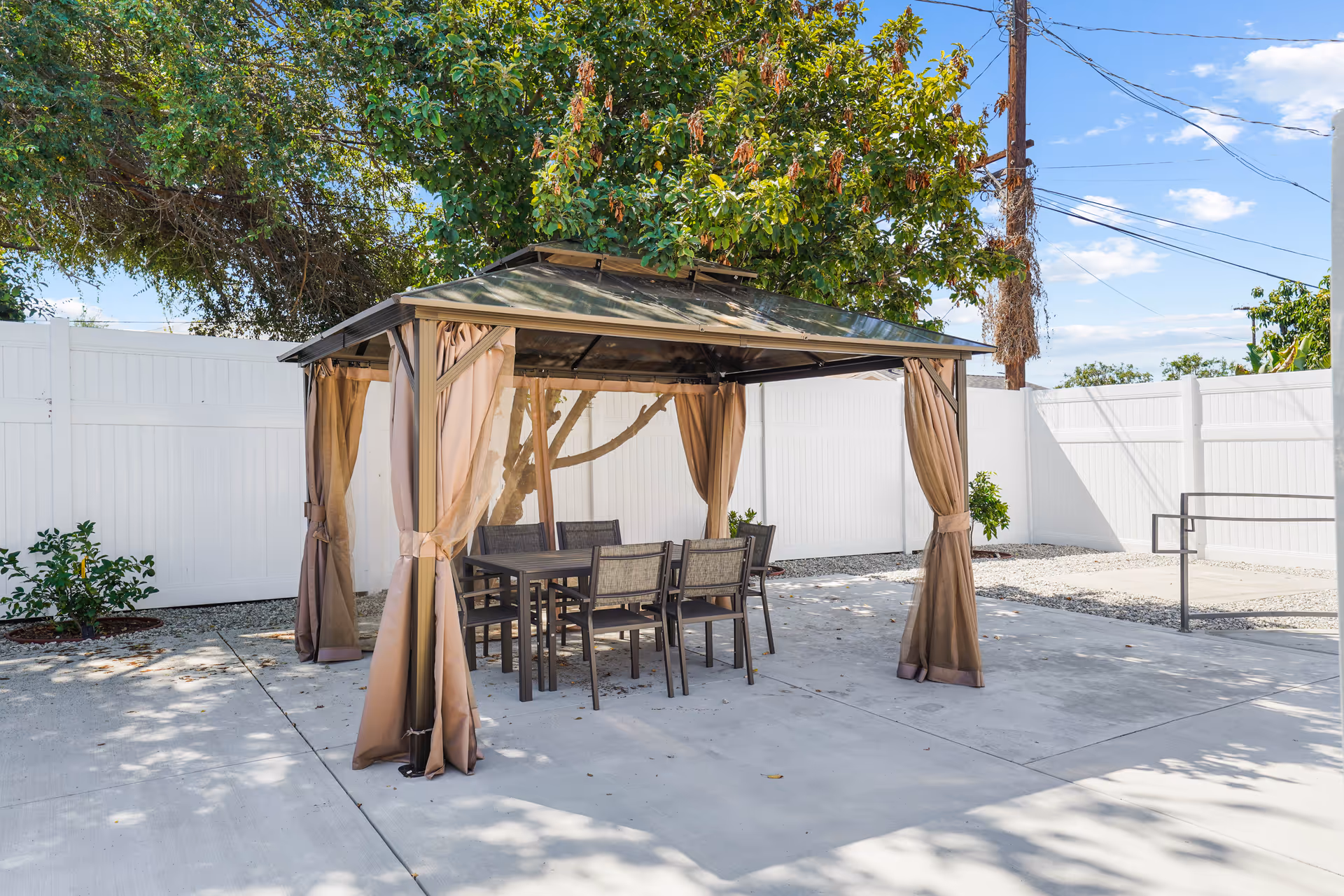 Outdoor patio with a gazebo, curtains, and dining table surrounded by chairs.