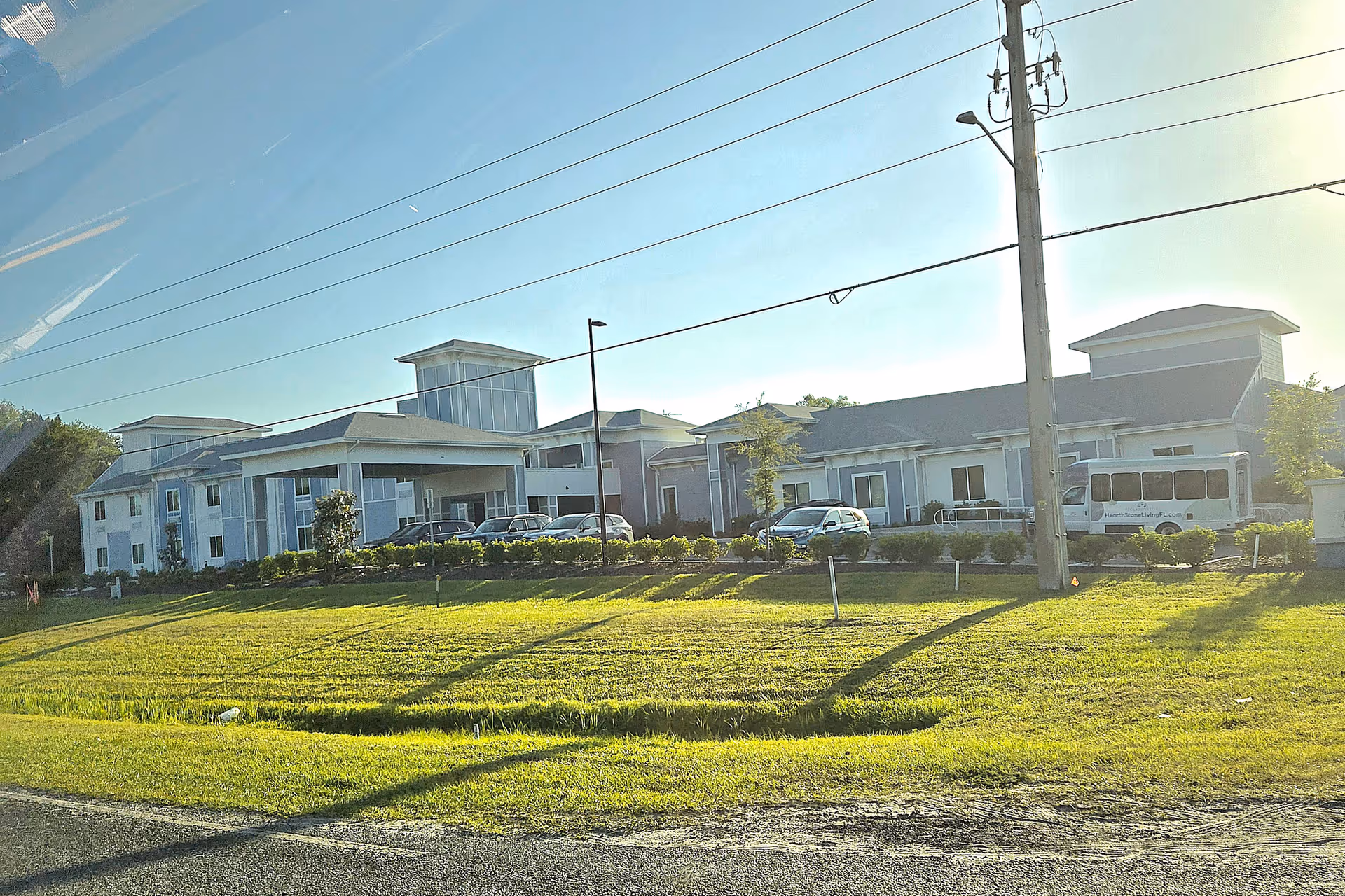 Exterior view of HearthStone at Leesburg building with parked cars, a bus, and green lawn.