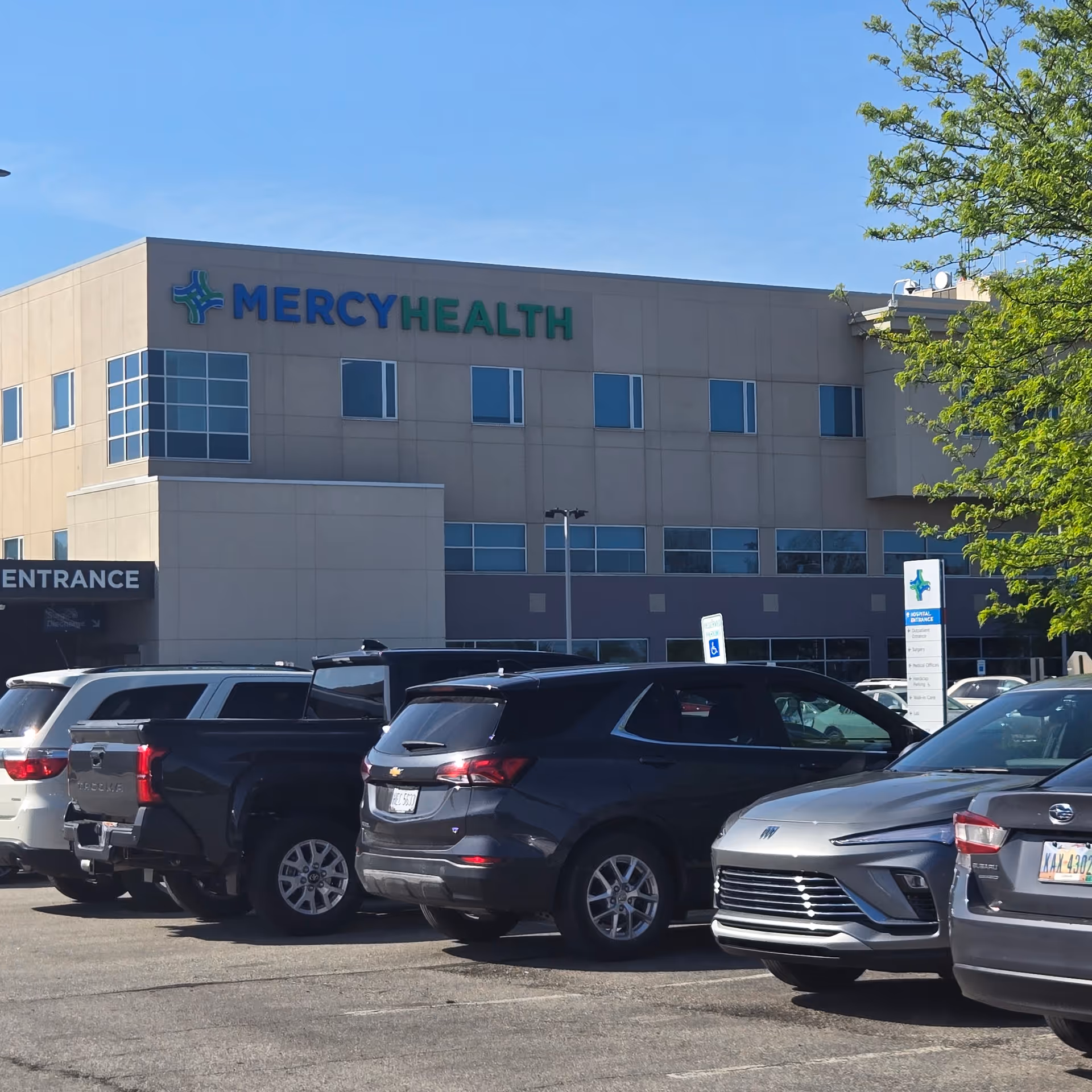Exterior view of Mercy Health Lorain Hospital with a parking lot and blue sky.
