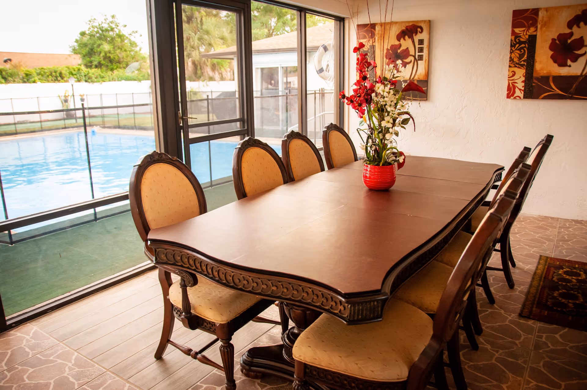 Long wooden dining table with chairs inside, overlooking a pool through glass walls.