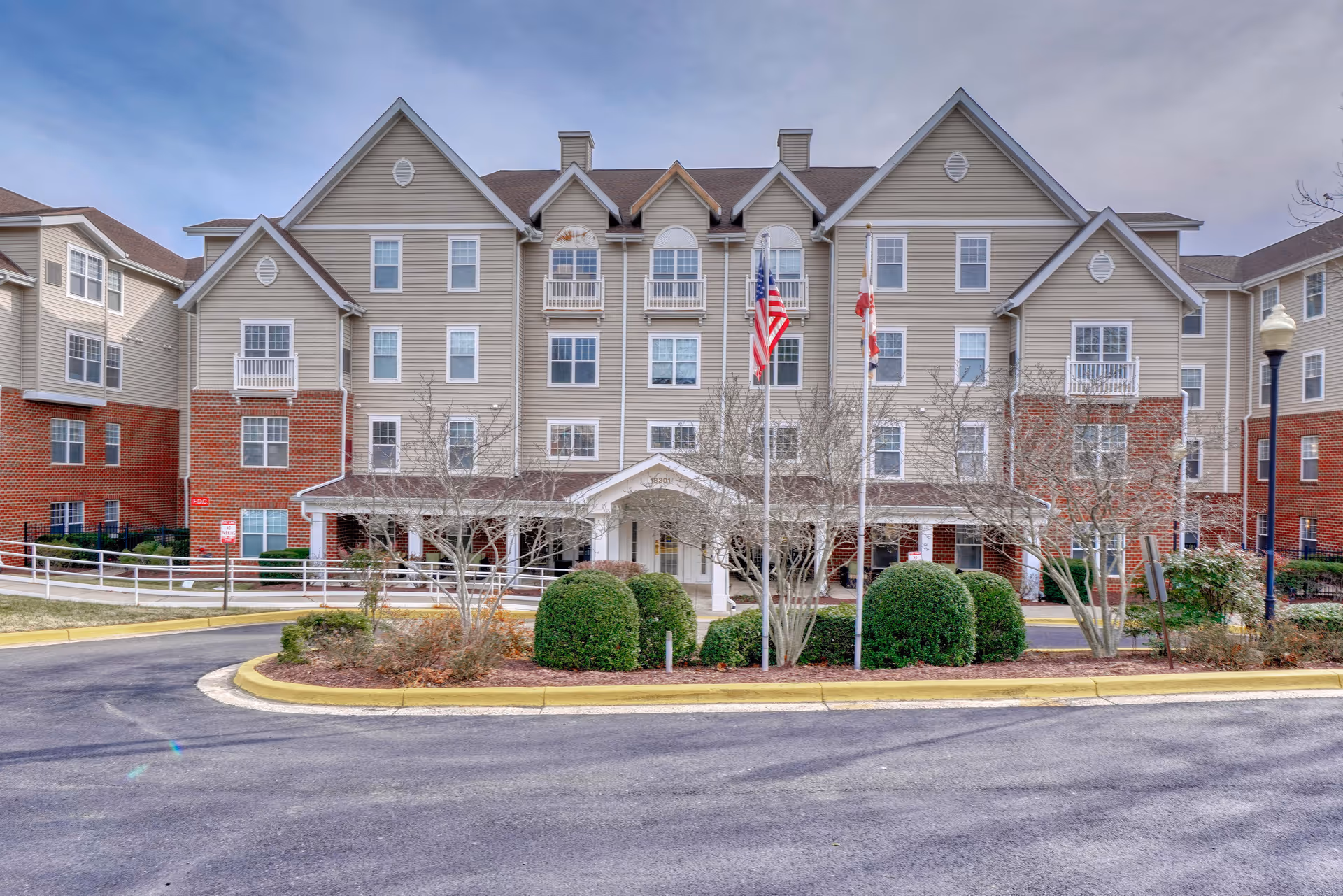 Front view of Willow Manor at Fair Hill Farm, a multi-story beige building with flags.