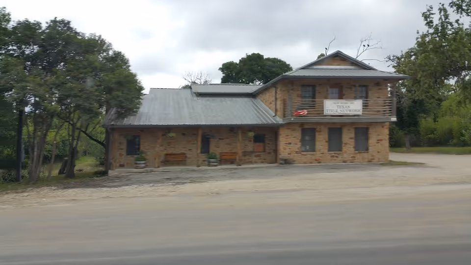 A small stone building with a metal roof beside a road; no people visible.