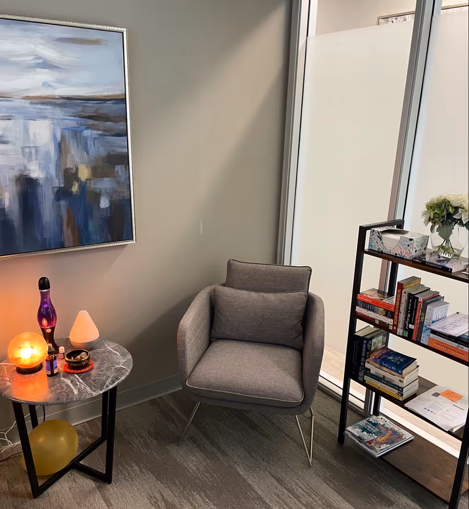 Cozy interior seating area with gray armchair, marble side table, bookshelf, and large window.