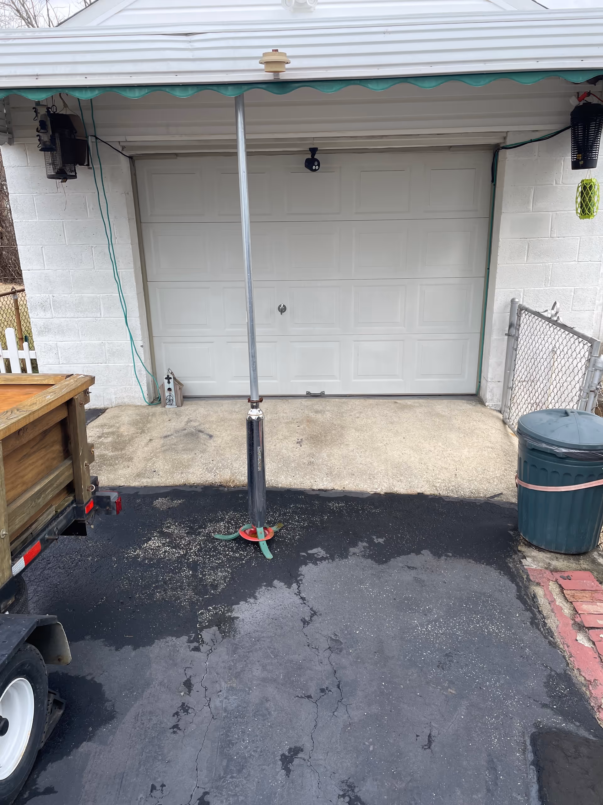 Exterior view of a building with a closed garage door, driveway, trash can, and equipment.