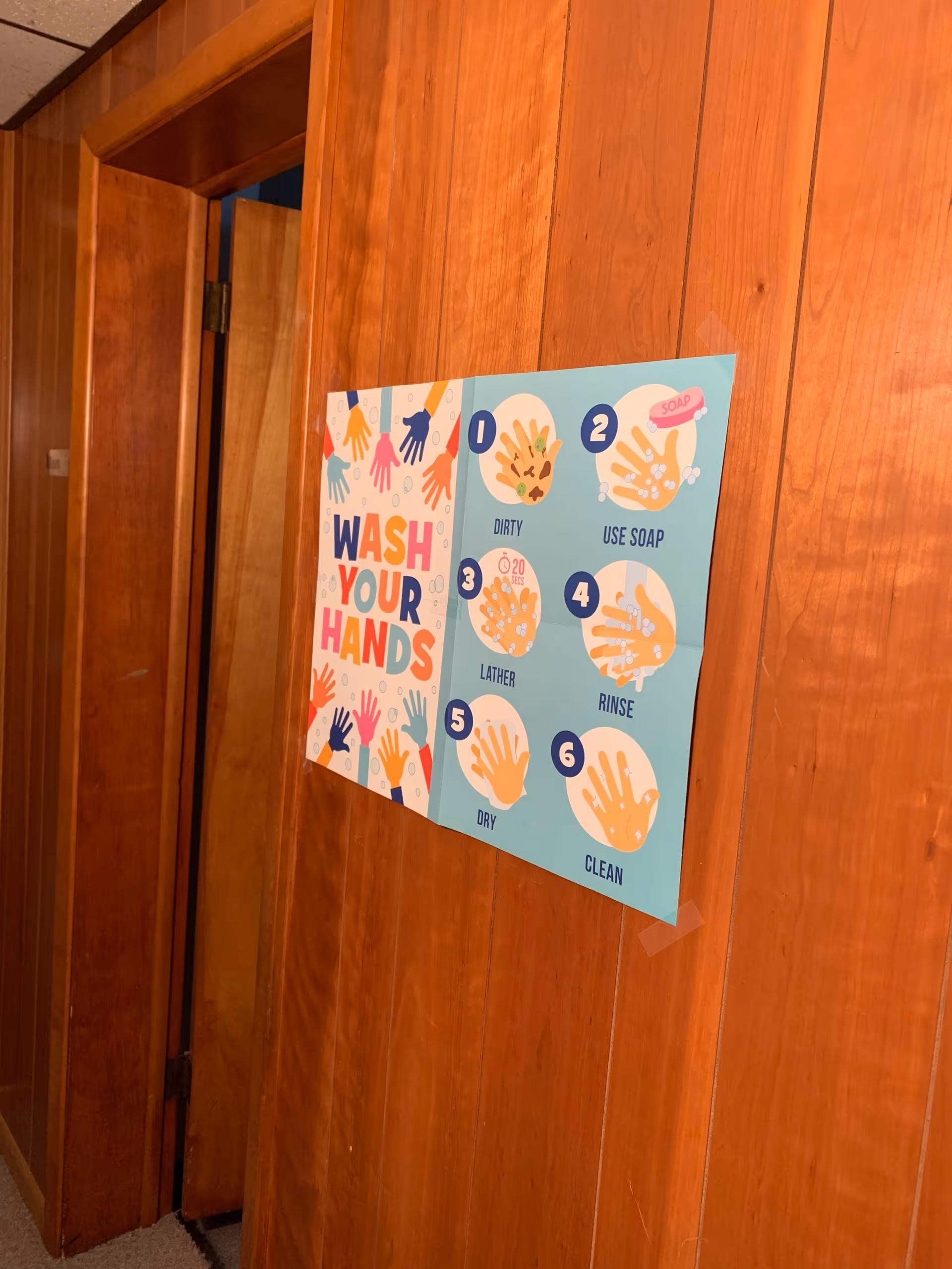 Poster detailing handwashing steps mounted on a wood-paneled interior hallway wall.