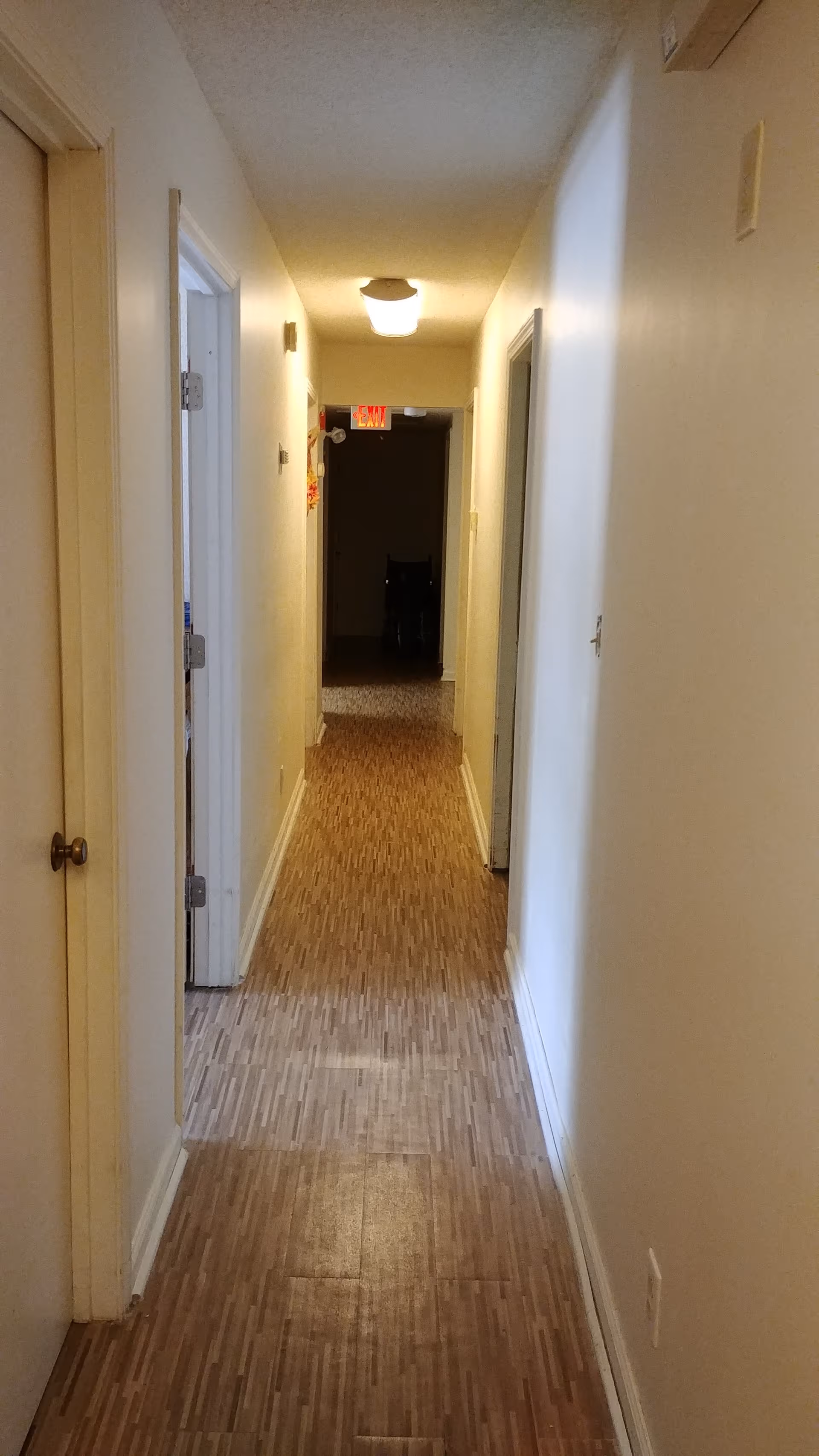 A long indoor hallway with doors on both sides and a lit ceiling.