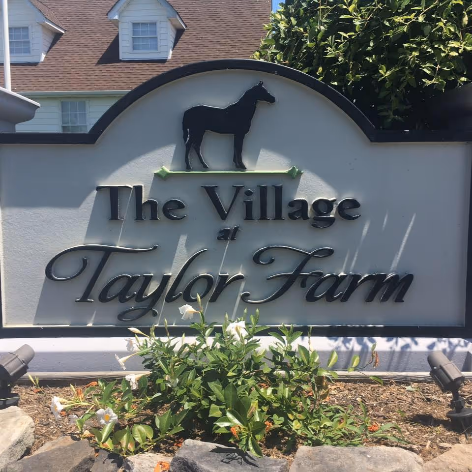 A sign for The Village at Taylor Farm with a horse silhouette and plants.