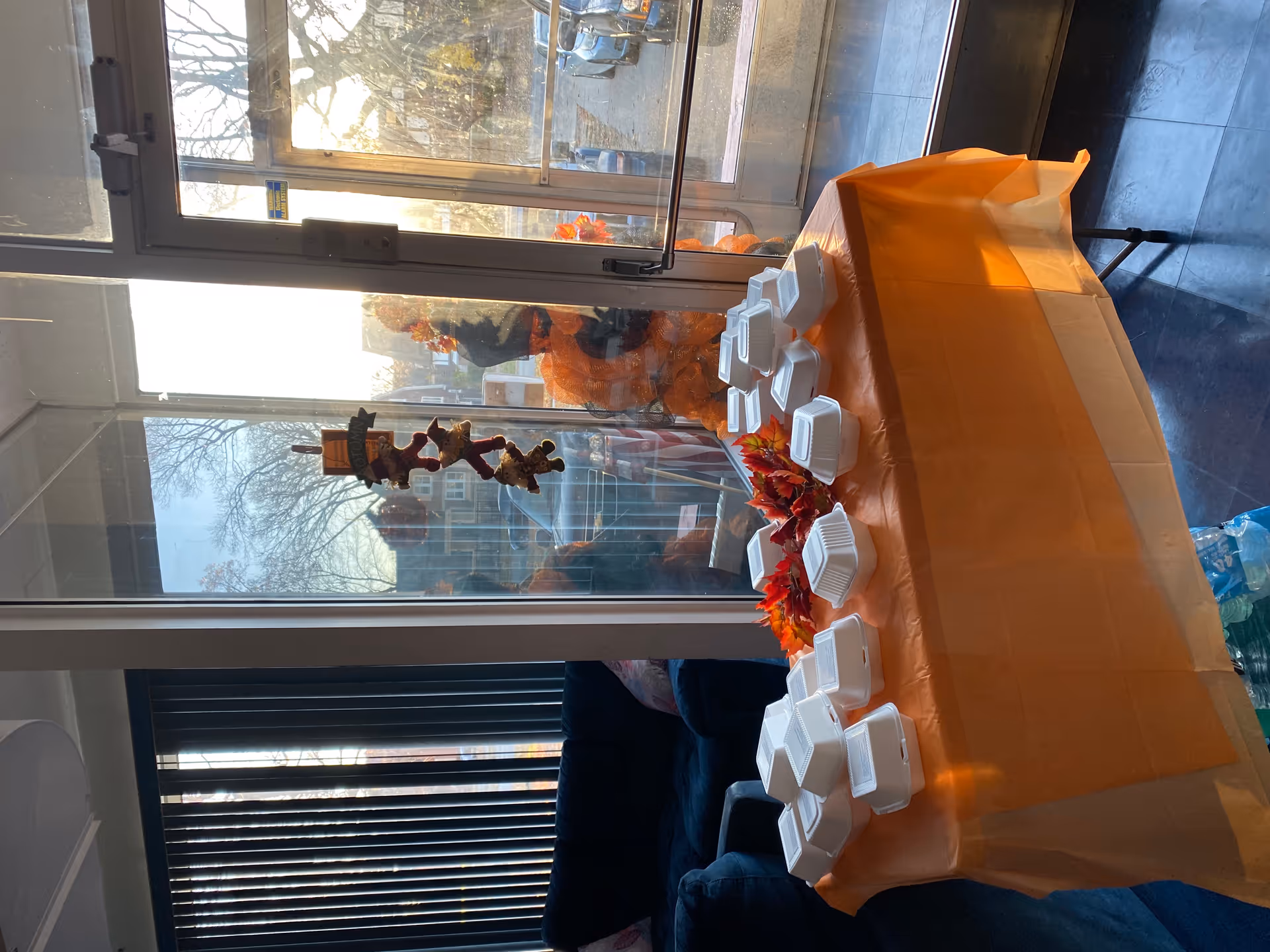 An indoor dining table with orange tablecloth and multiple white takeout containers, autumn decor.
