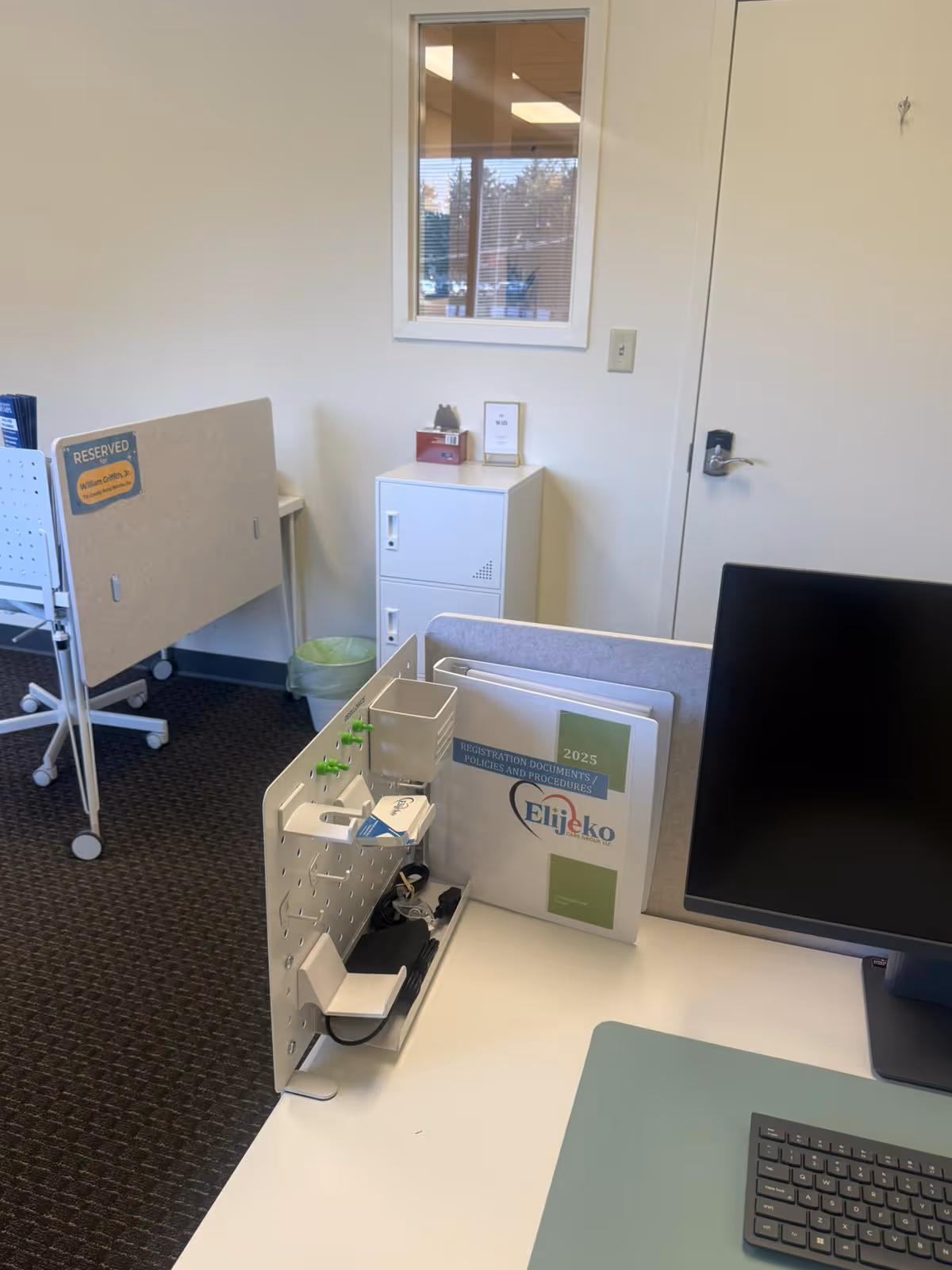 Office workspace inside a senior care facility, featuring a desk, computer, file organizers, and window.
