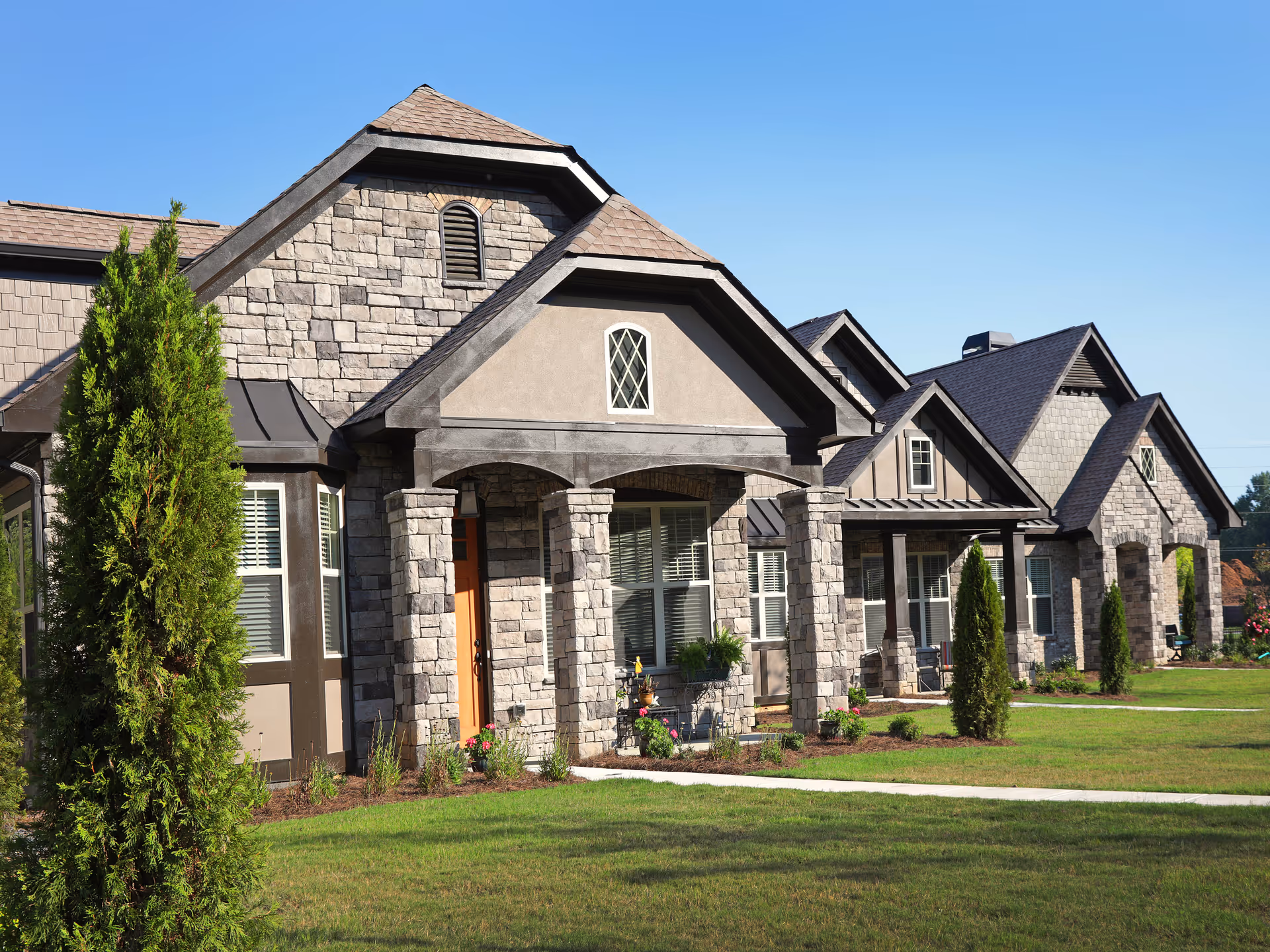 Row of stone-faced senior living cottages with porches and trimmed lawns under a clear blue sky.