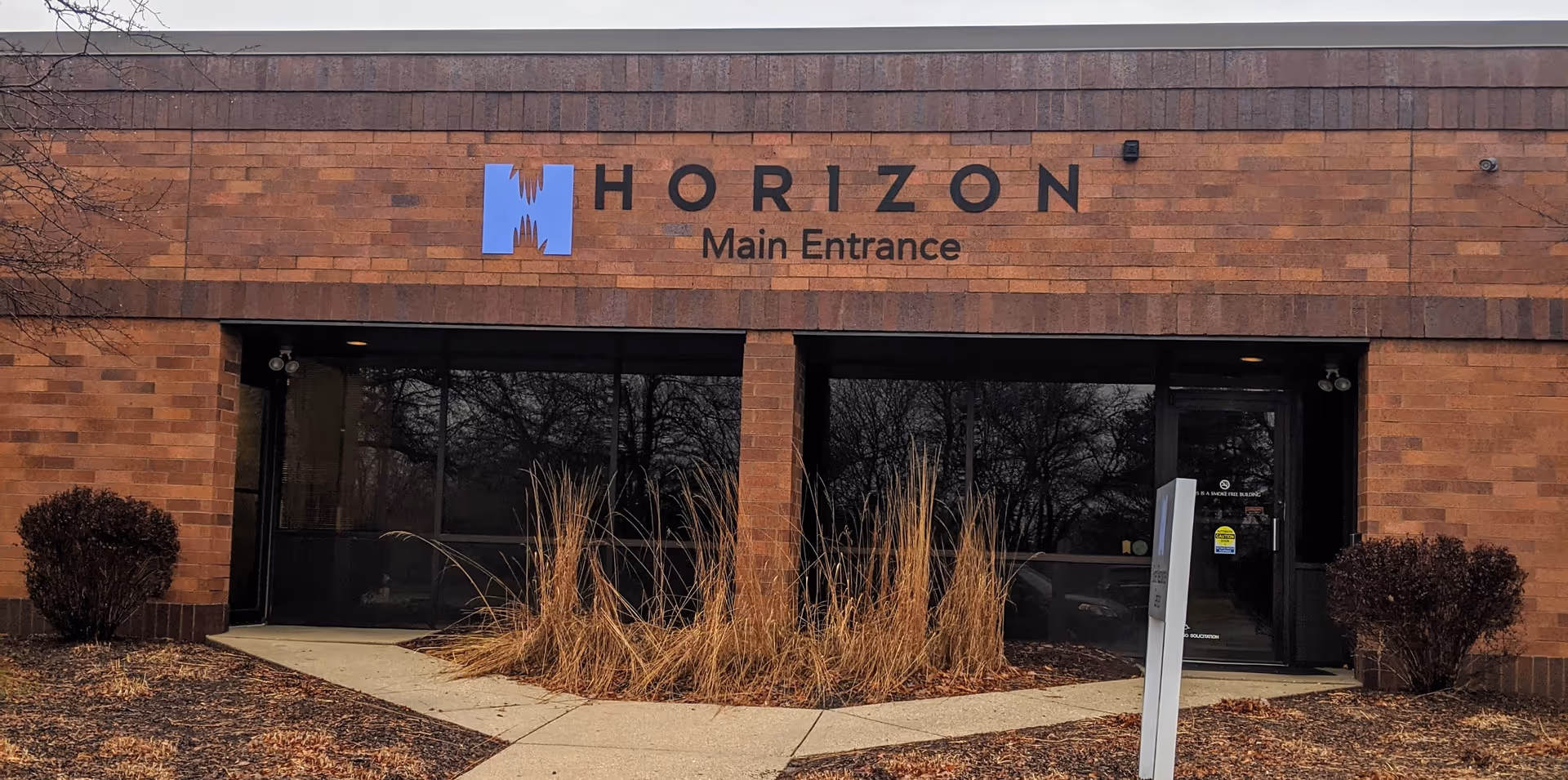 Brick facade of Horizon Main Entrance with glass doors and landscaping.