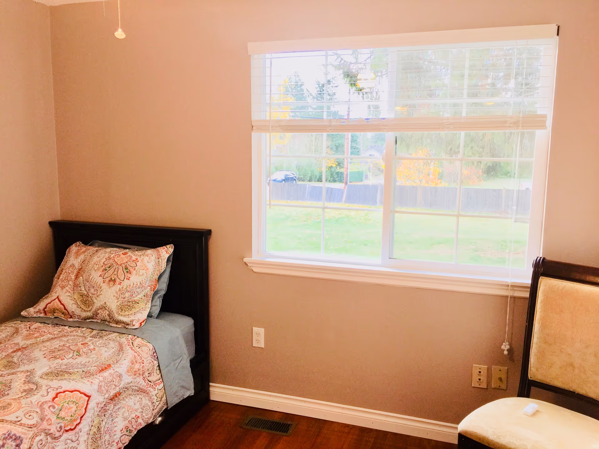 Cozy bedroom with a dark wood bed, paisley bedding, and a large window with blinds.