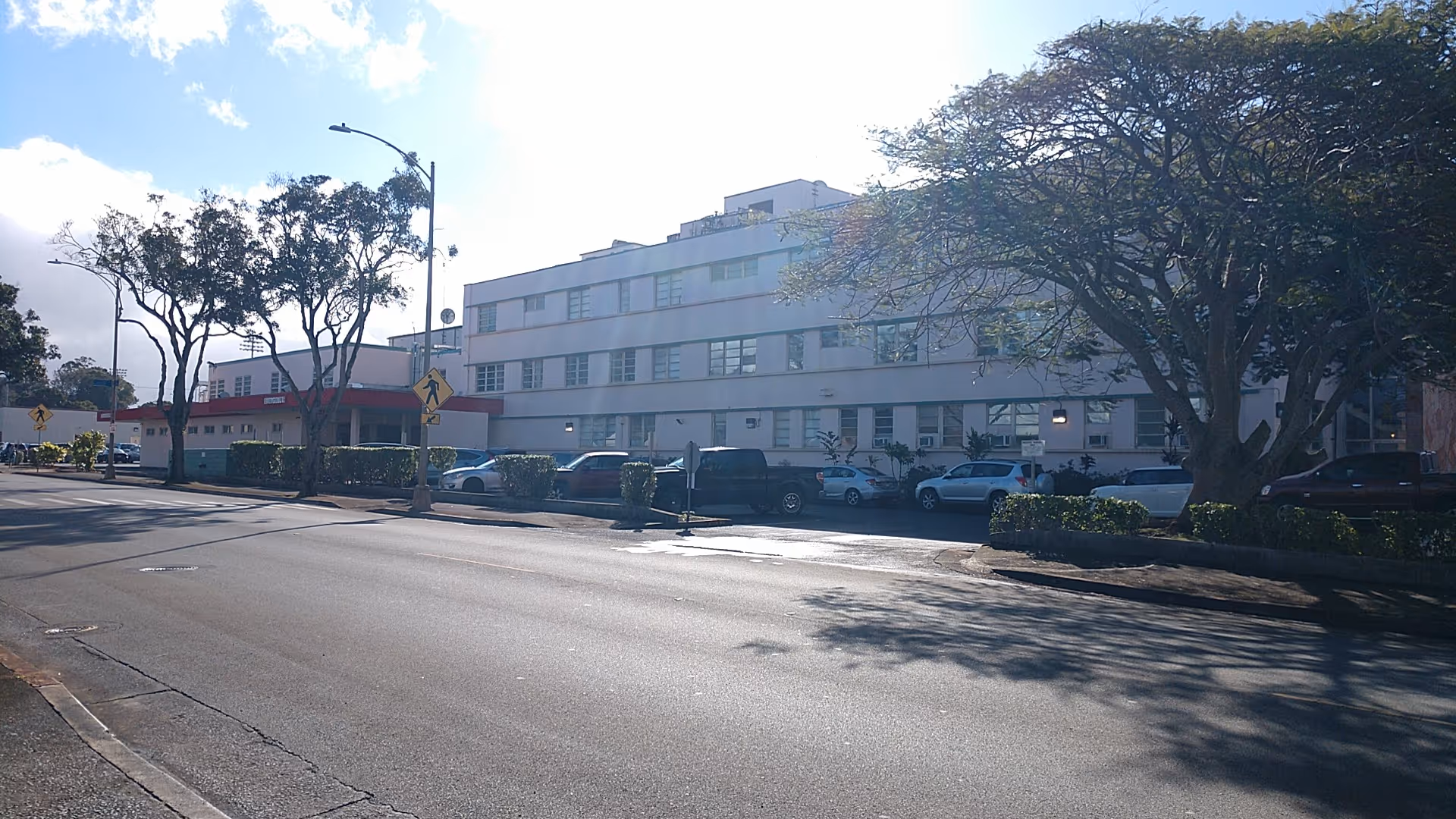 Exterior view of a multi-story senior living facility with parked cars and trees.