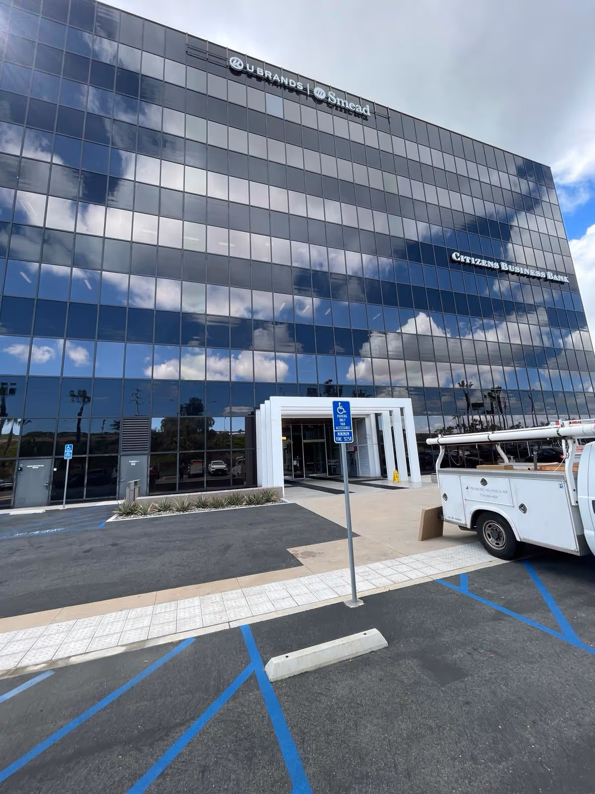 Tall glass office building exterior with entrance and handicap parking sign