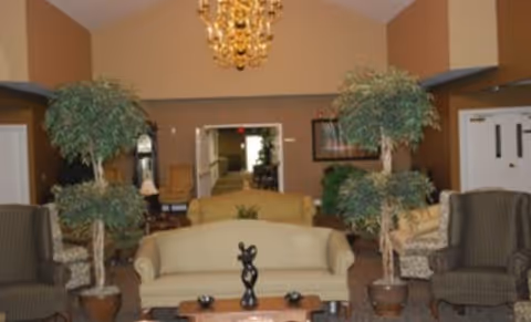 A seating lounge with sofas, armchairs, potted trees, a coffee table and a chandelier.