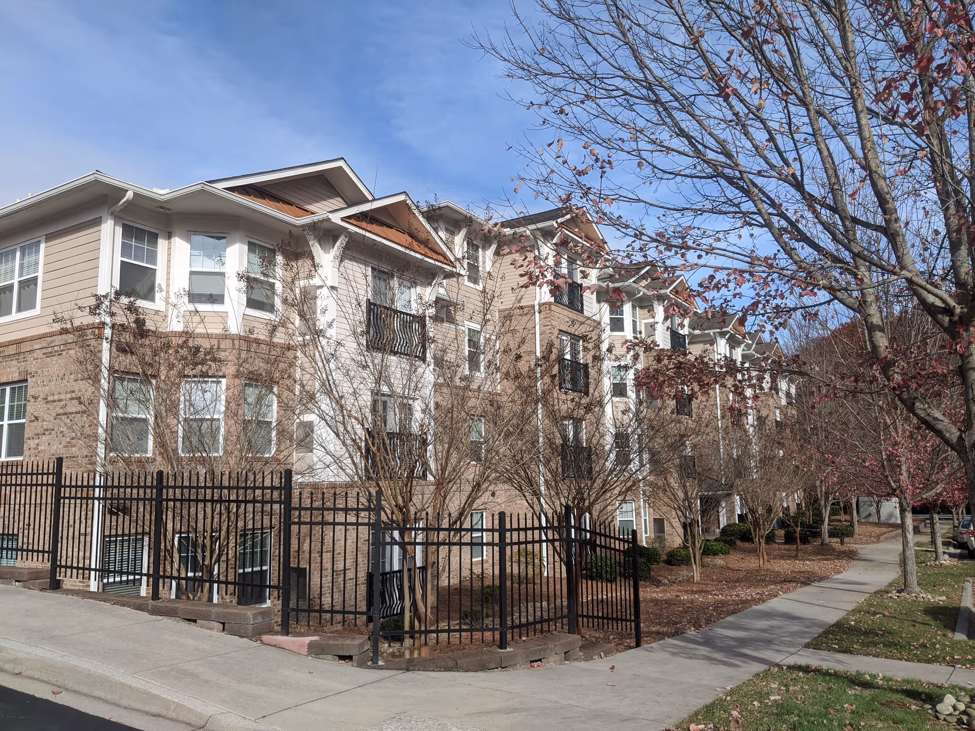 Exterior view of a multi-story senior living building with trees along a sidewalk.