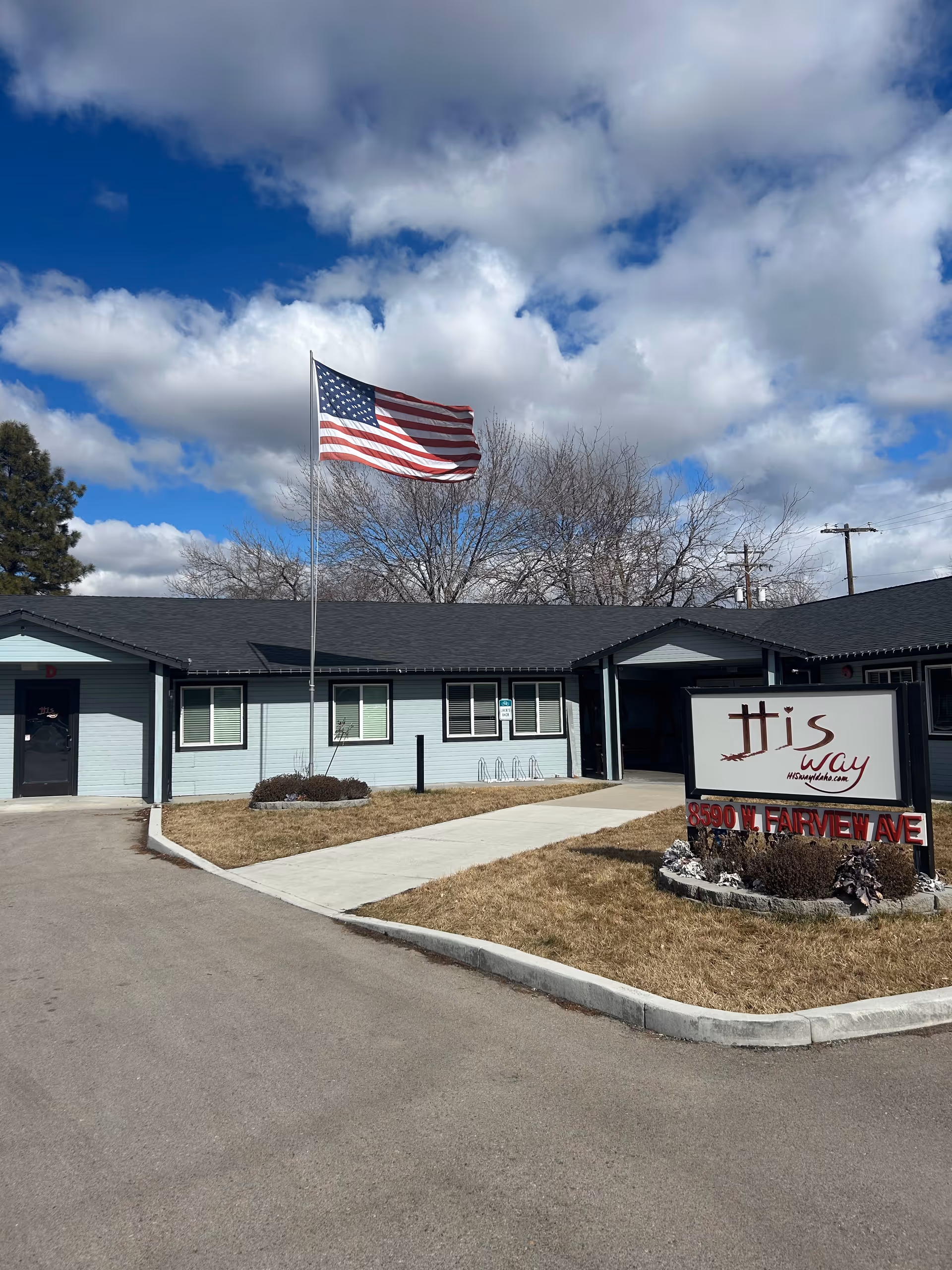 Front exterior of a single-story senior living facility with an American flag and sign.