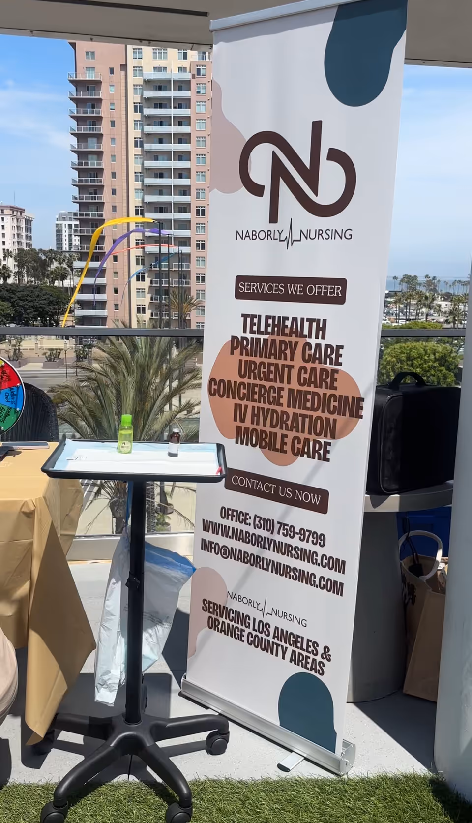 Outdoor promotional banner for Naborly Nursing with table, bottle, and city high-rises in background.