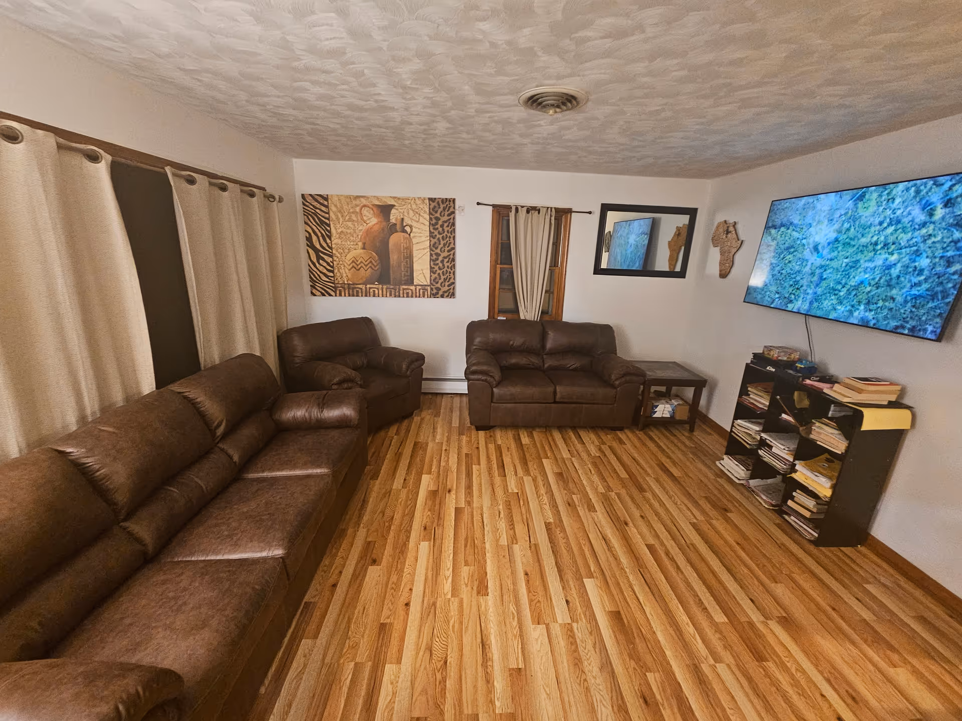 Cozy living room with brown leather sofas, a mounted TV, and a bookshelf.