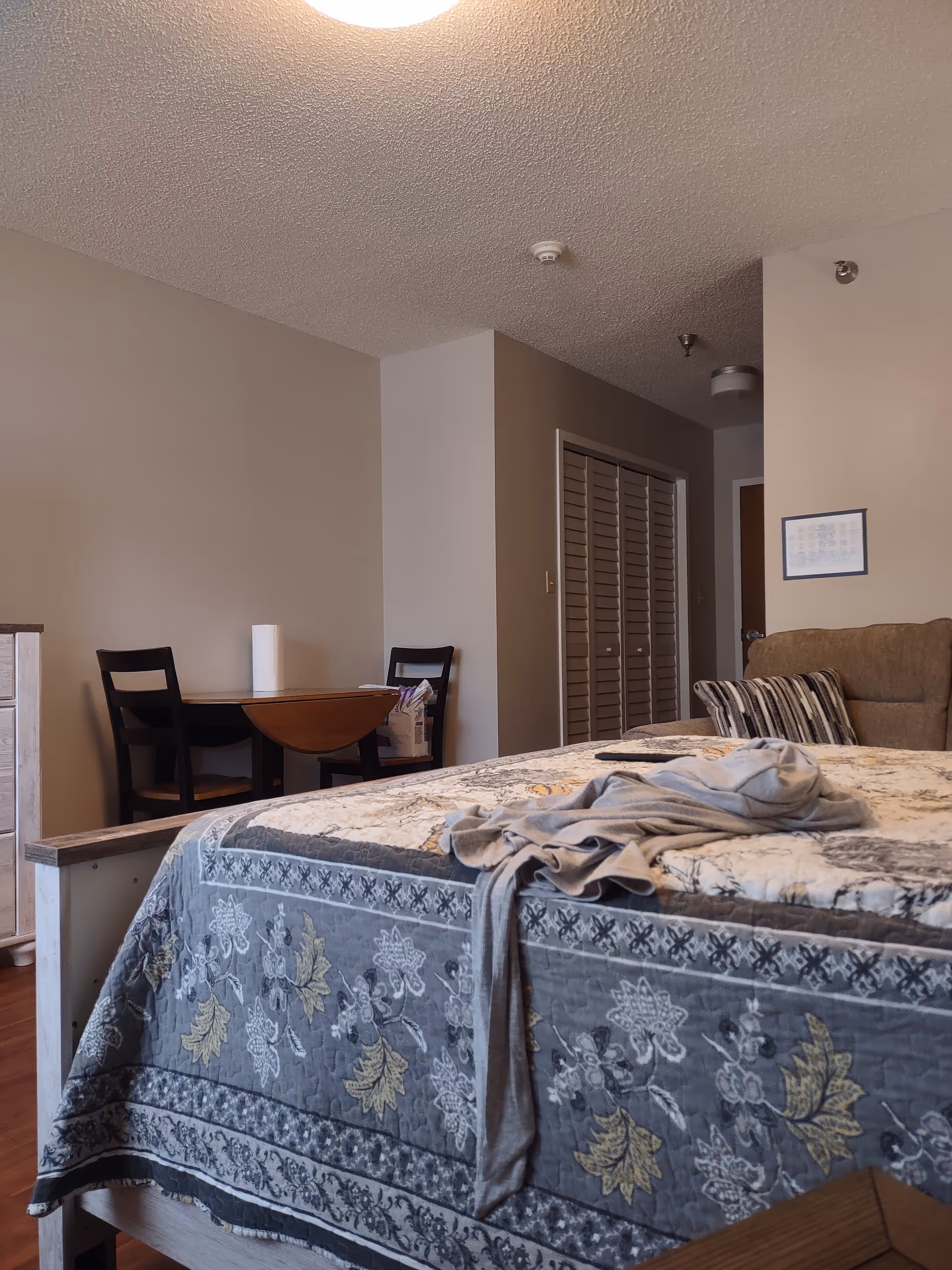 A bedroom in Hilltop at Glenwood with a bed, dresser, and small table with chairs.