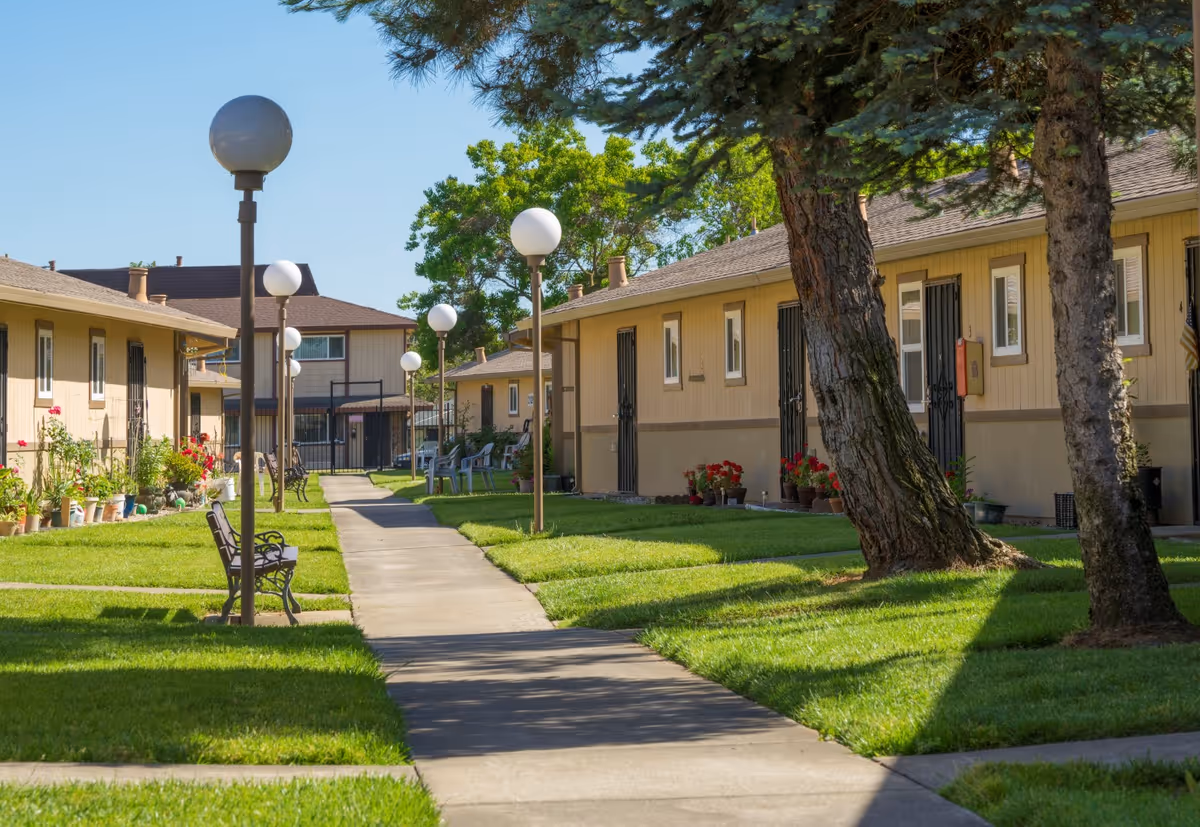 Sunny courtyard of a senior housing complex with lawns, walkway, and benches.