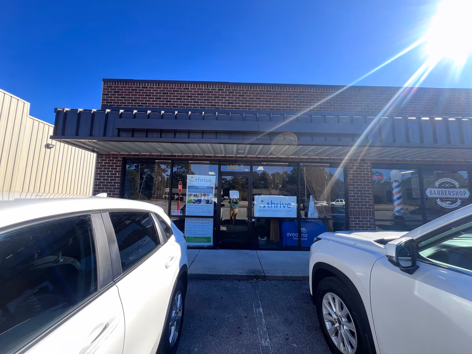 Front view of Aveanna Healthcare facility with brick exterior, glass doors, and parked cars.