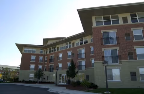 Exterior view of a multi-story brick senior living building with a glass entrance.