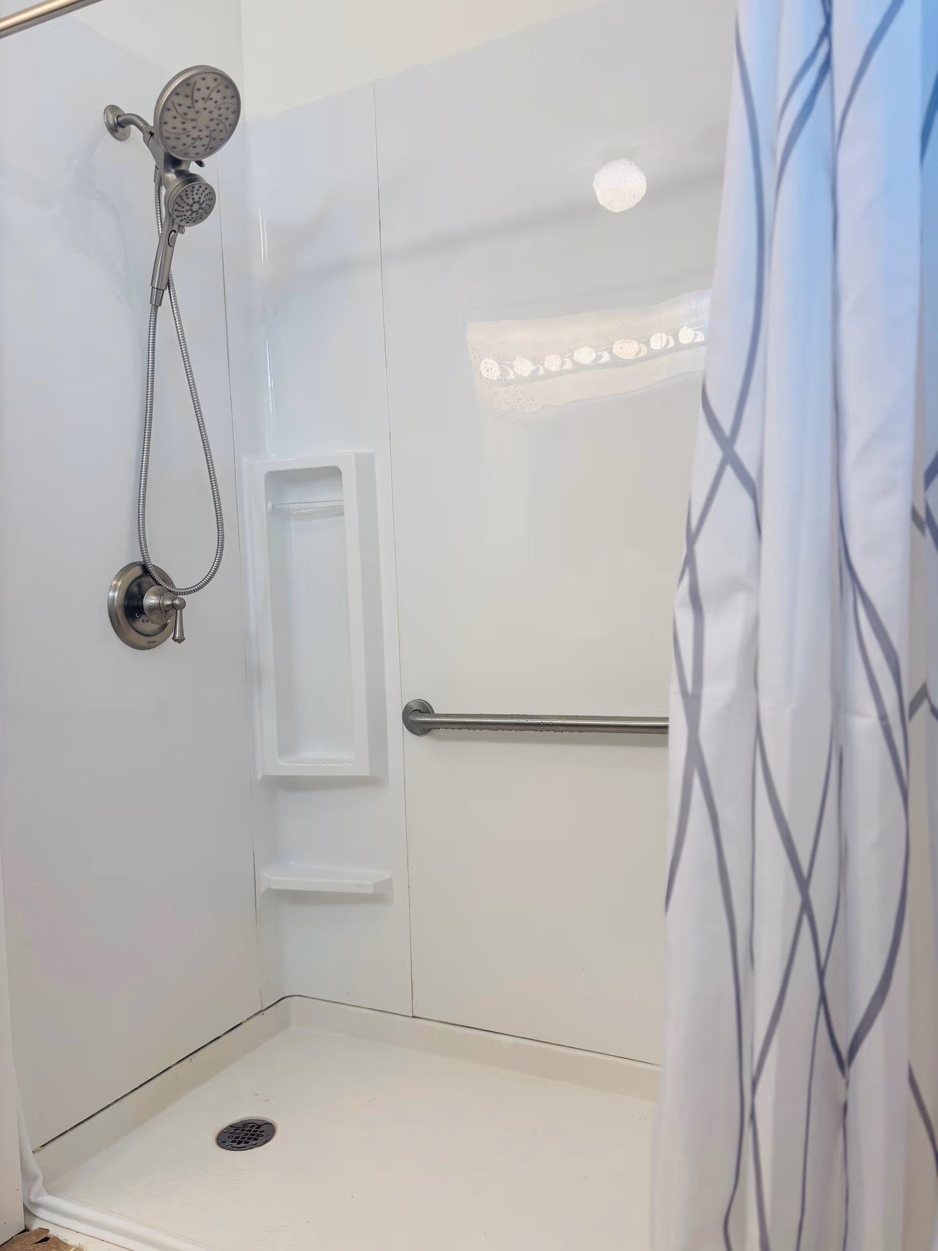 White walk-in shower with handheld nozzle, built-in shelf, grab bar, and striped curtain.