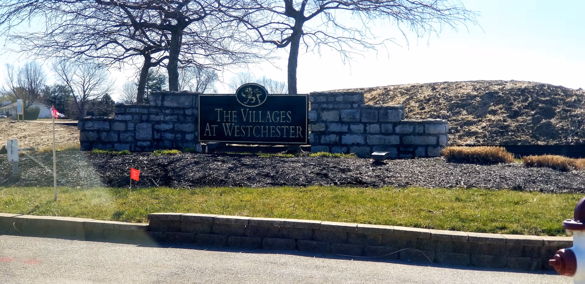 Entrance sign The Villages At Westchester behind a stone wall with landscaping.