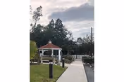 Outdoor pathway leads to a white gazebo with a red roof amid trees.
