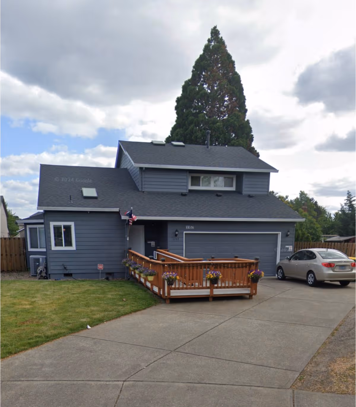 Blue-gray two-story home with a wooden ramp entrance, planters, and a parked car.