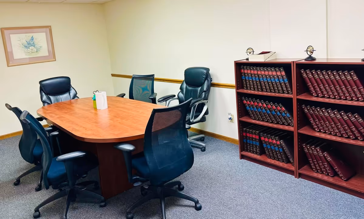 Conference room with a wooden table, chairs, and a tall bookshelf of binders.