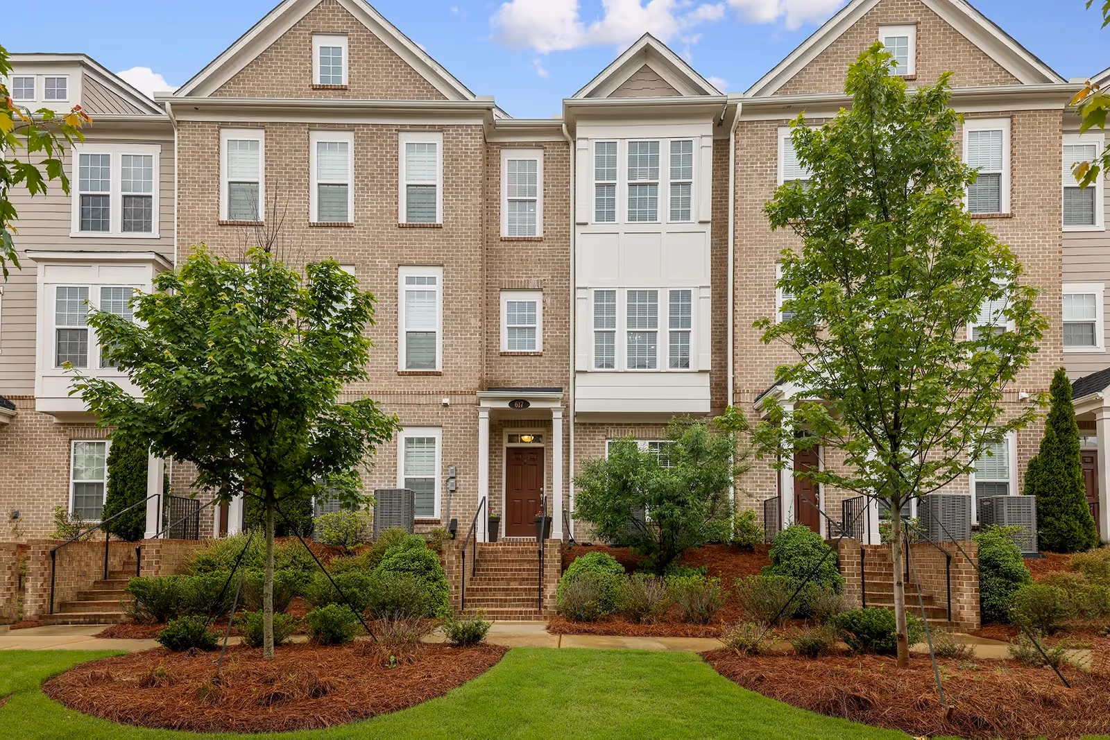 Row of brick, townhome-style senior living buildings with manicured landscaping and trees.