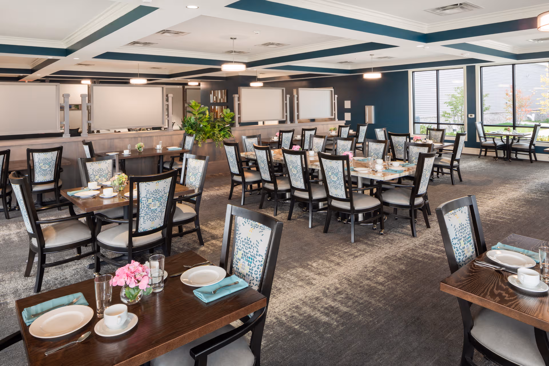 Spacious dining hall with multiple tables set for meals in a senior living facility.