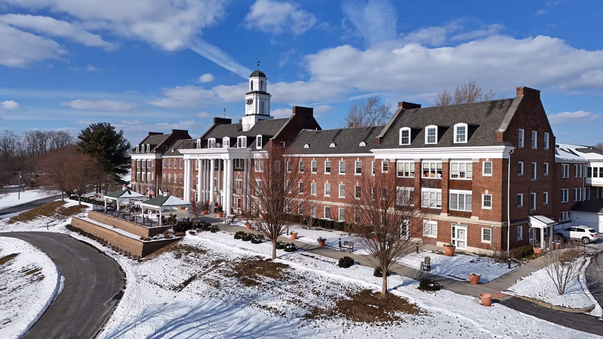 Brick senior living building with a central columned entrance, clock tower, and snow-covered grounds.