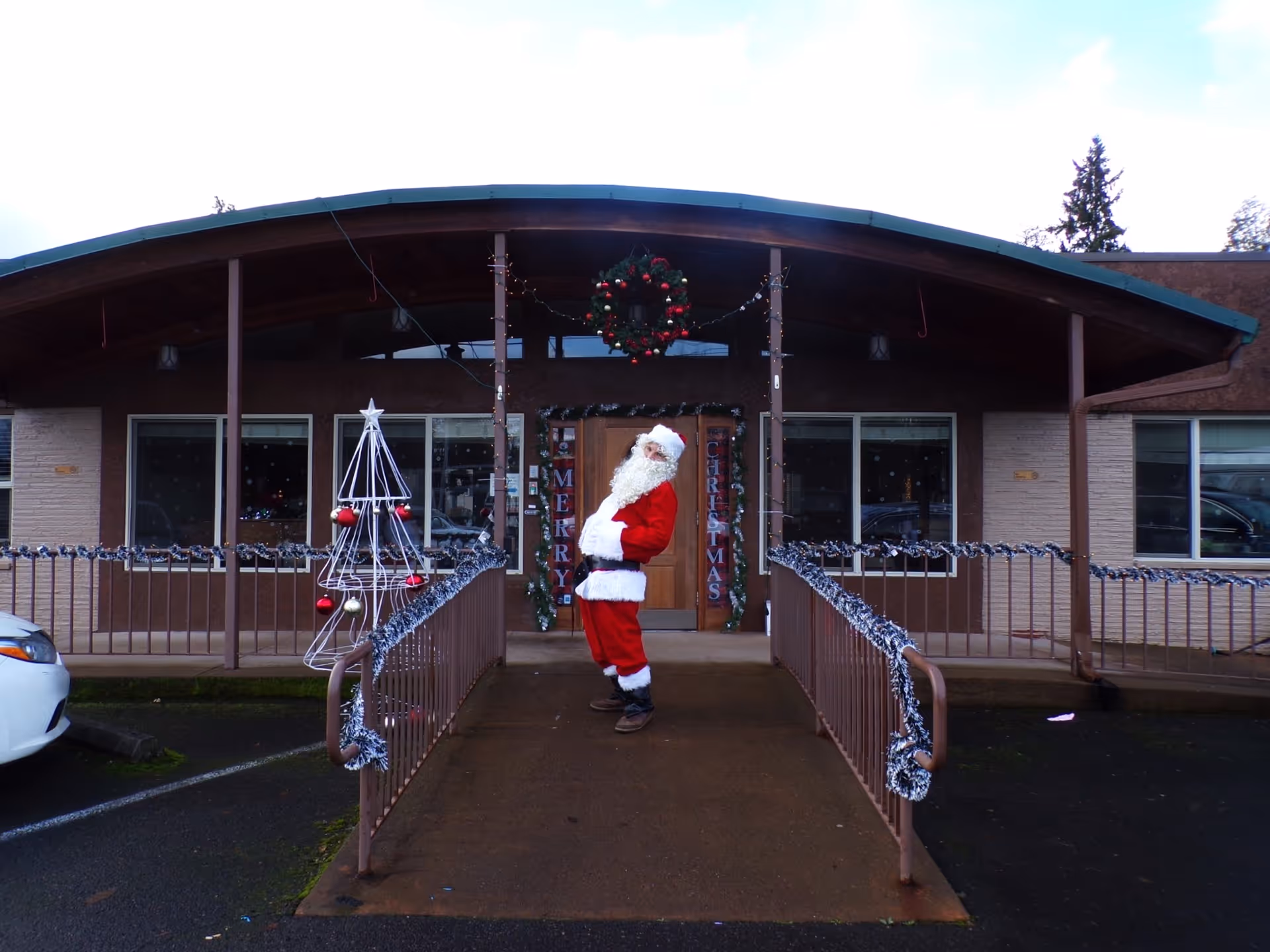 A person dressed as Santa Claus stands on a decorated entrance ramp outside the single-story facility's front entrance.